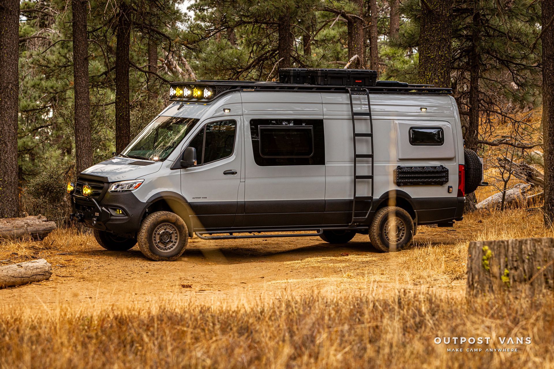 A camper van is parked in a field in the woods.
