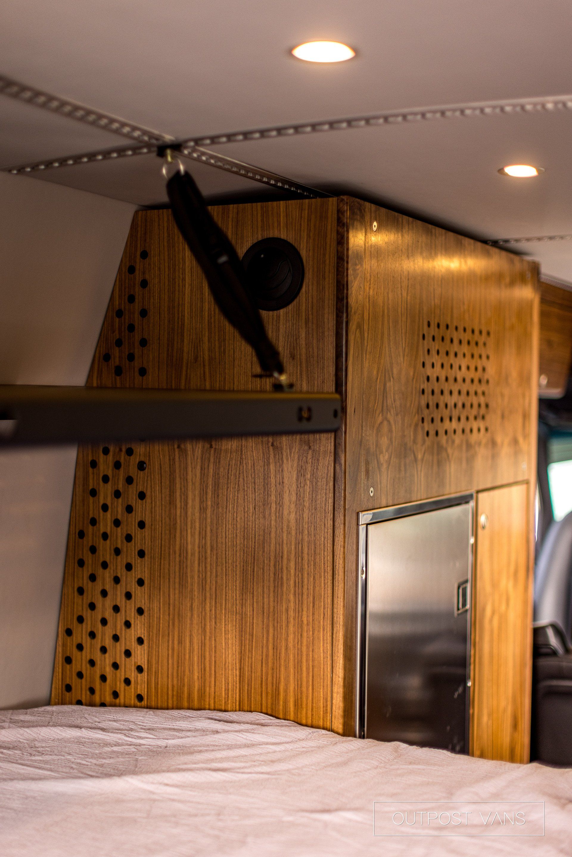 A camper van with a bed and a wooden cabinet.