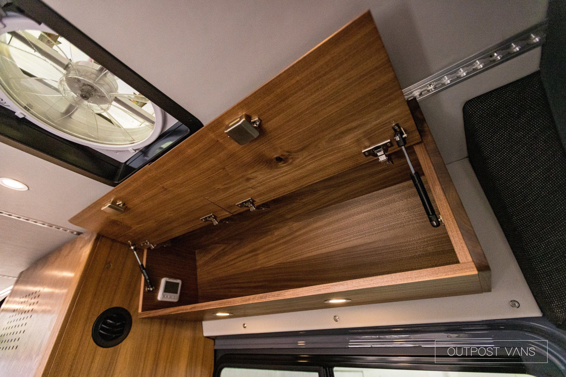 A wooden cabinet is open in a camper van.