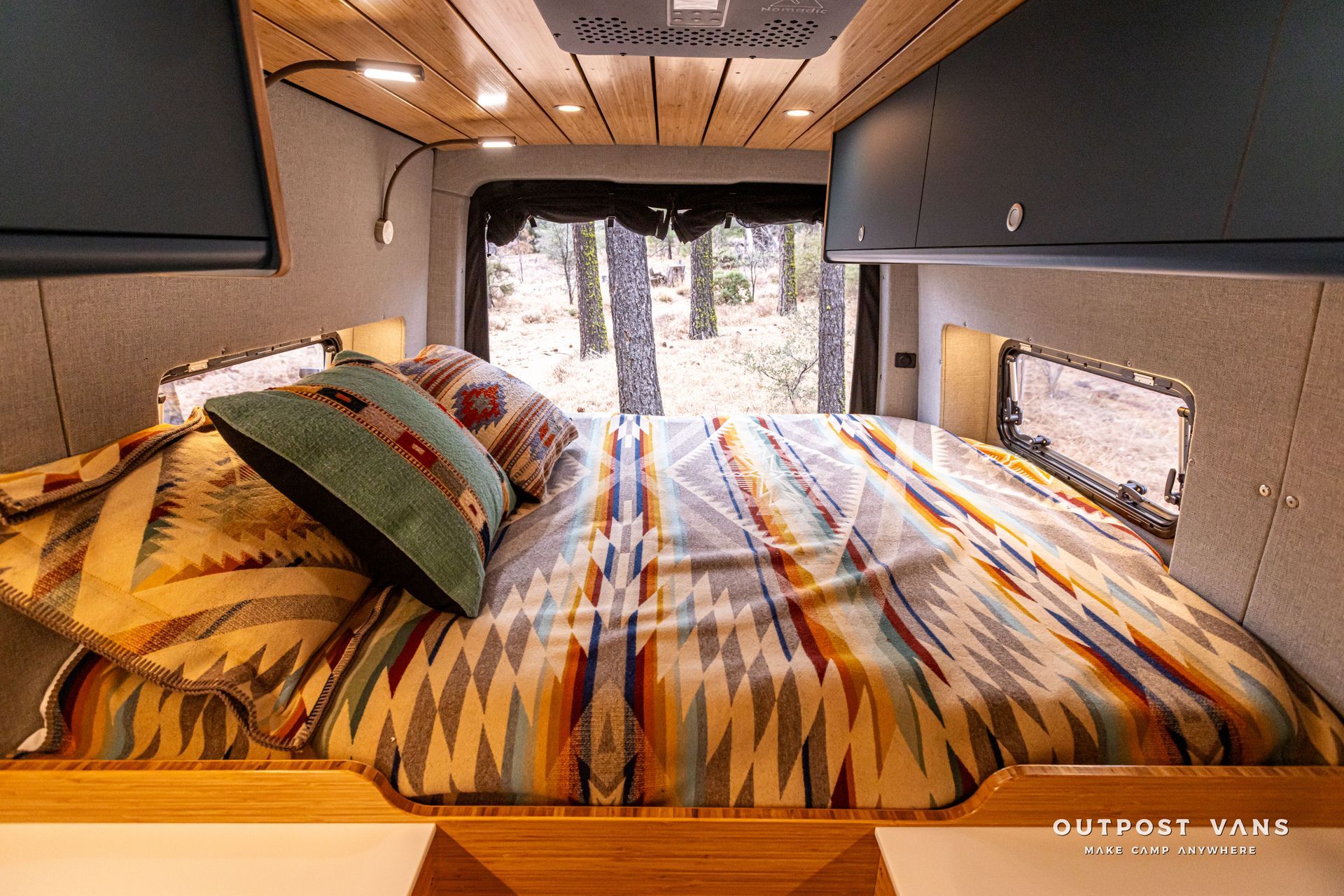 A bed with a colorful blanket and pillows in a camper van.