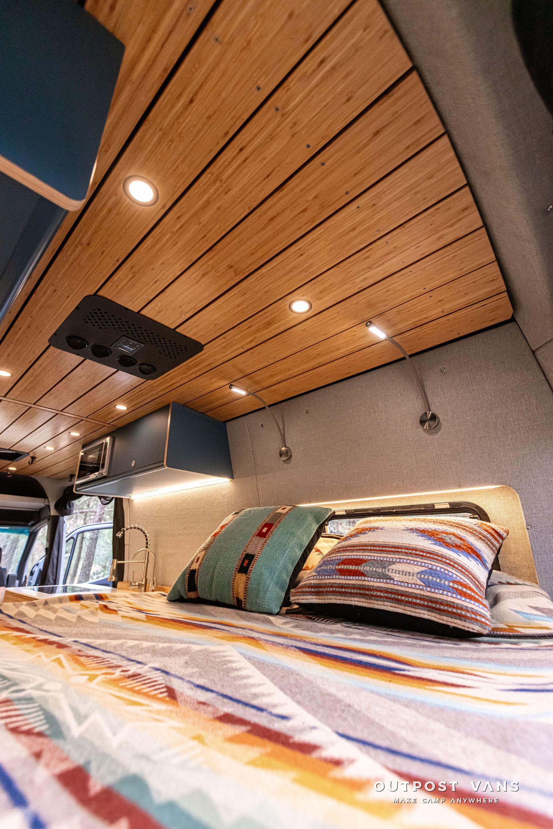 There is a bed in the back of a van with a wooden ceiling.