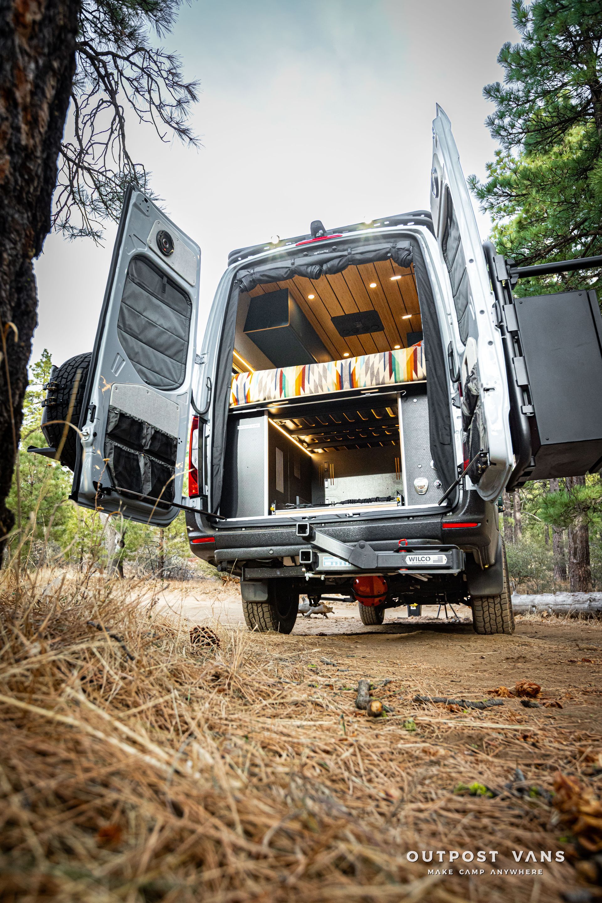 A van is parked in the woods with its doors open.