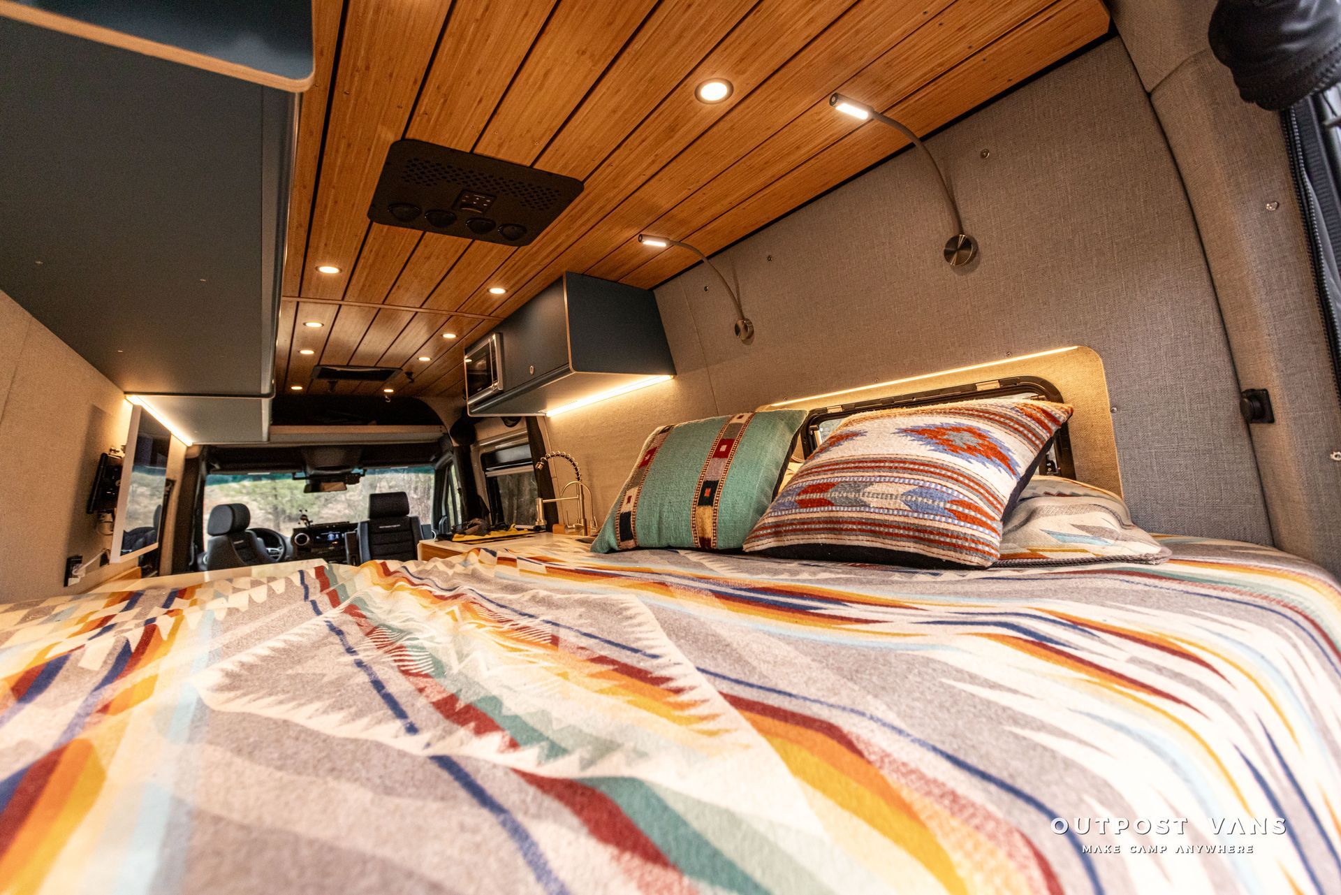 A bed in the back of a van with a blanket on it.