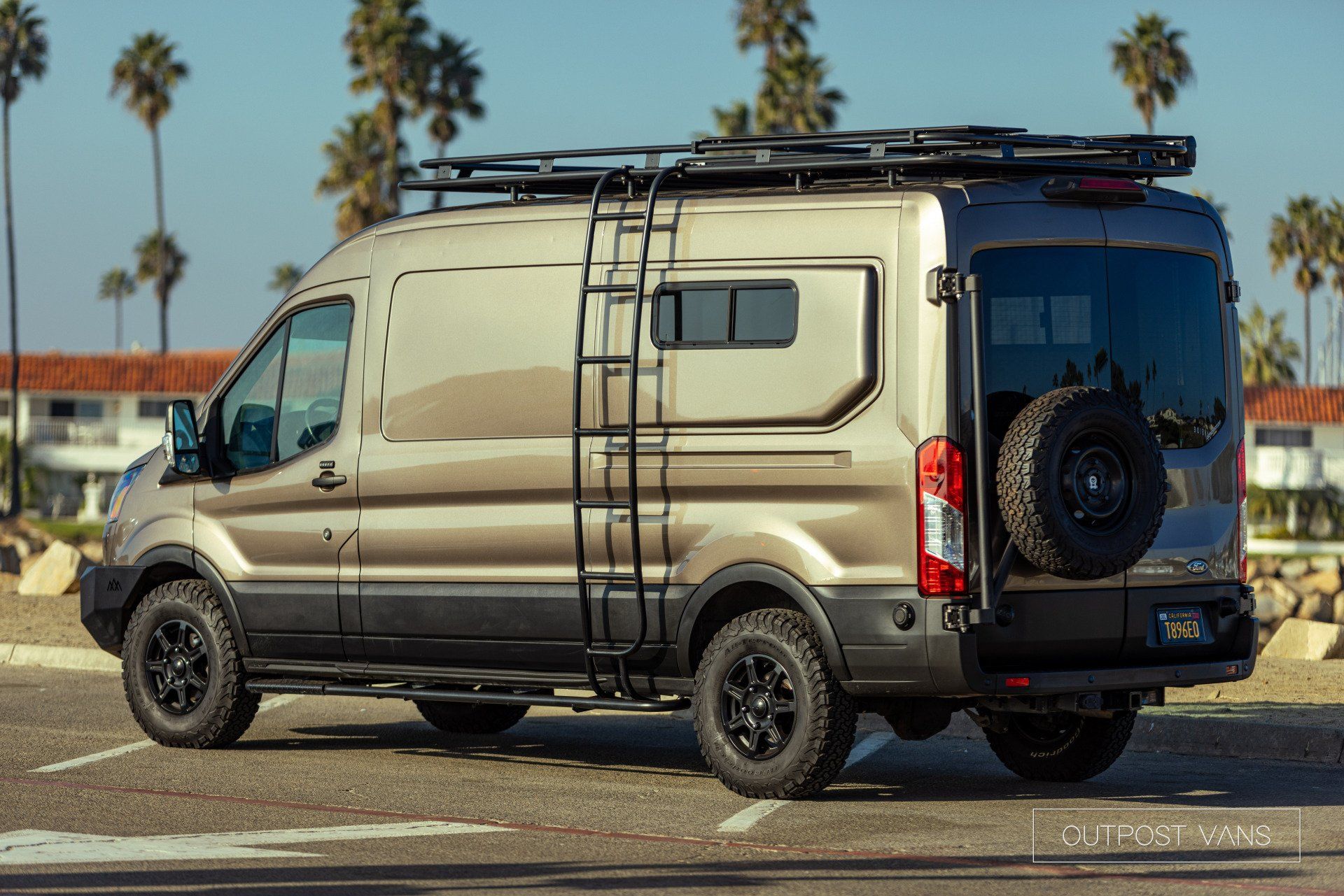 A van with a ladder on top of it is parked in a parking lot.