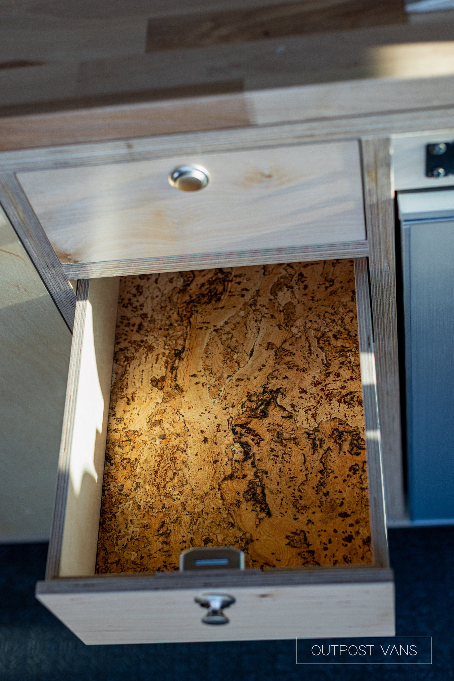 a wooden drawer with a cork bottom is open in a kitchen .