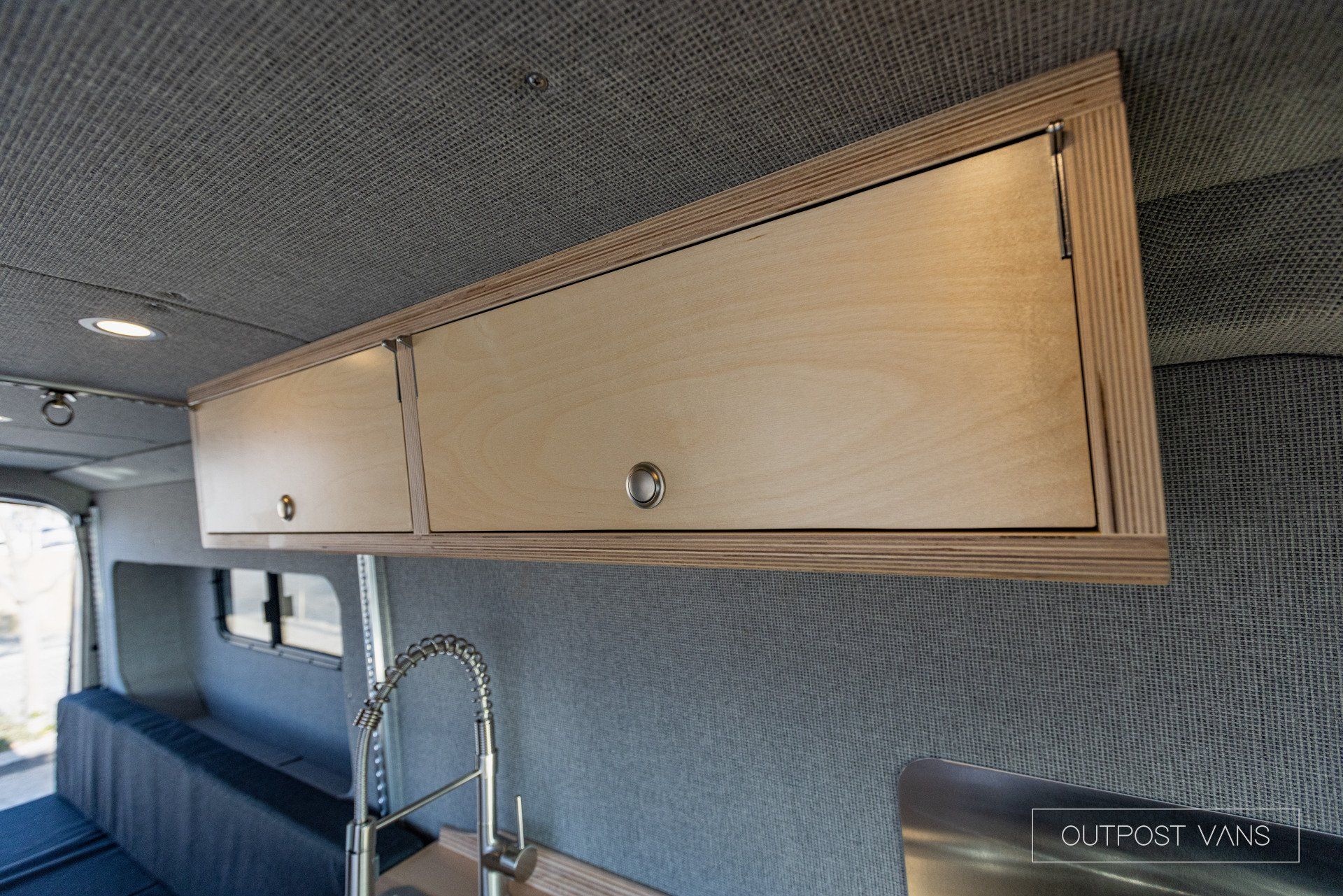 a kitchen in a van with a sink and cabinets above it .