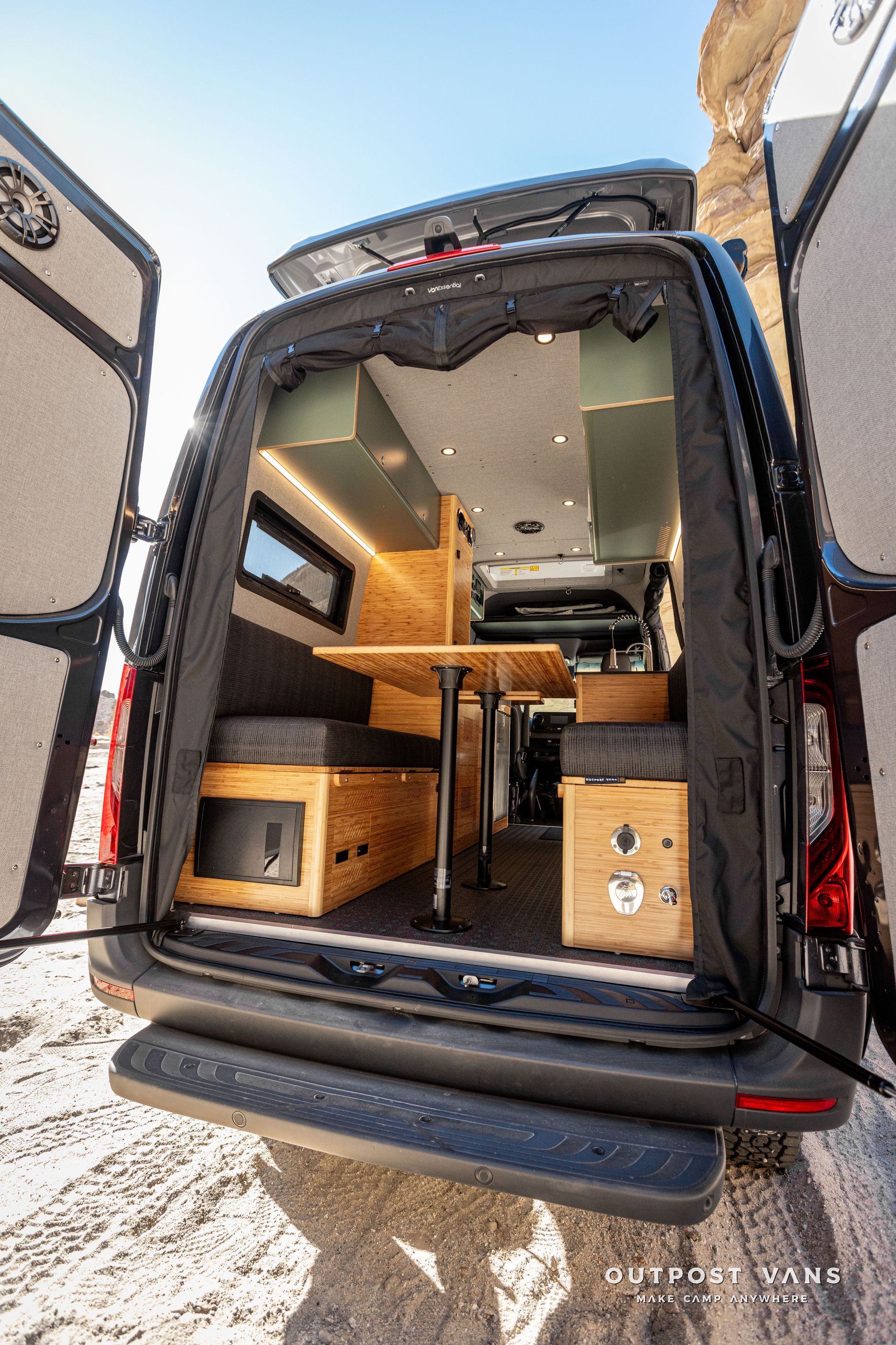 The inside of a camper van with a dinette table and benches that convert to a bed. outdoor shower
