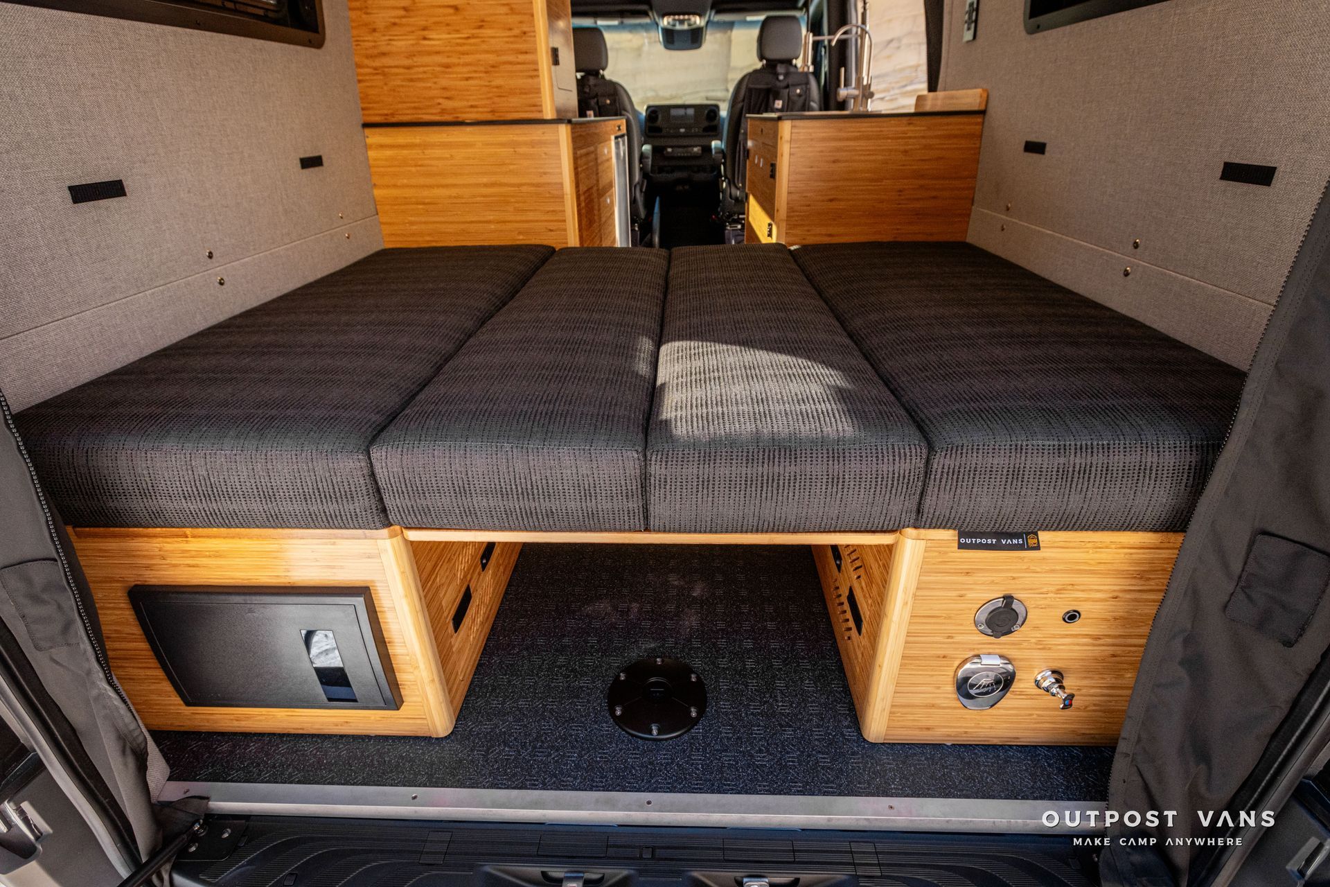 The back of a van with its doors open and a dinette converted bed in the back.