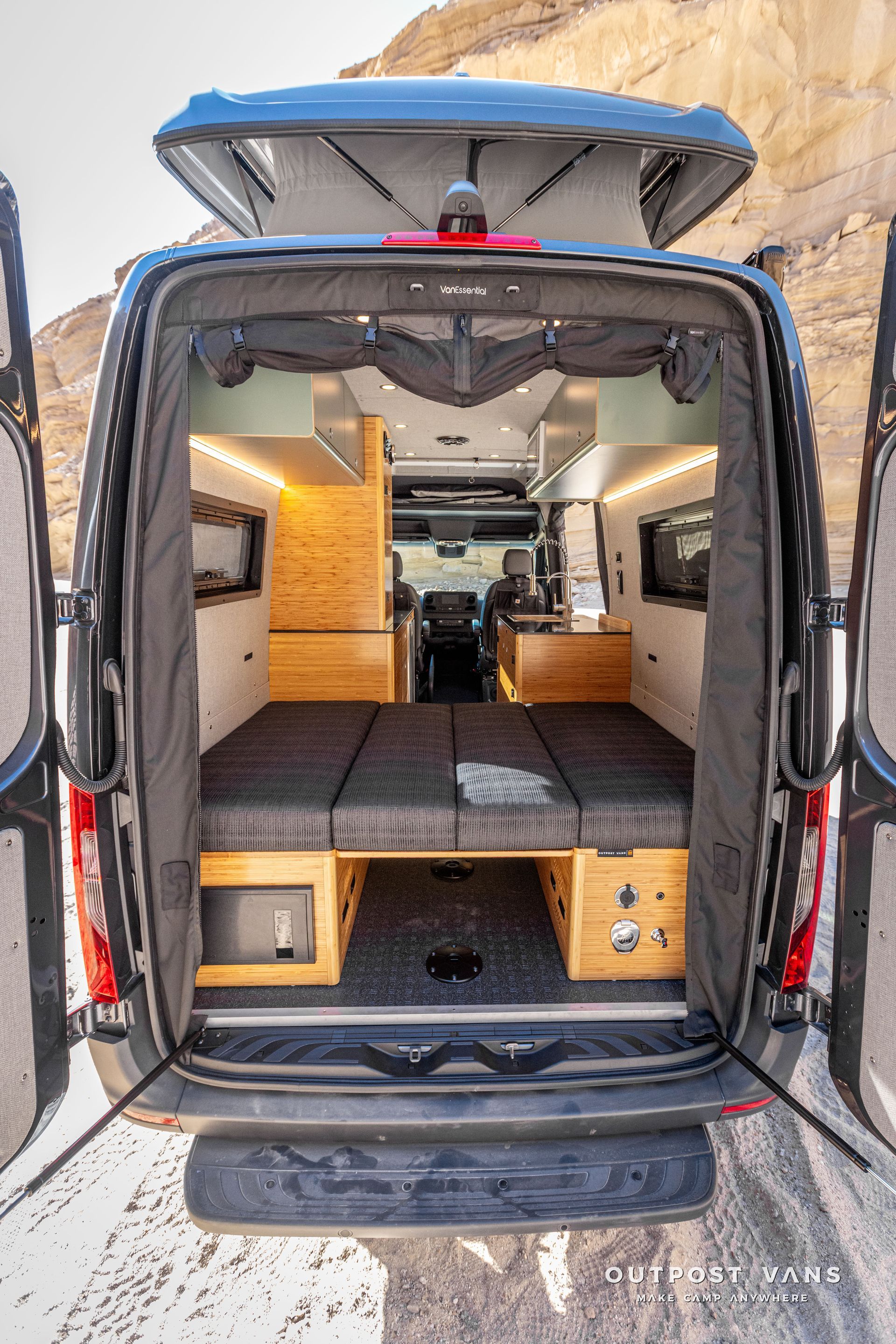 The back of a van with its doors open and a dinette converted bed in the back.