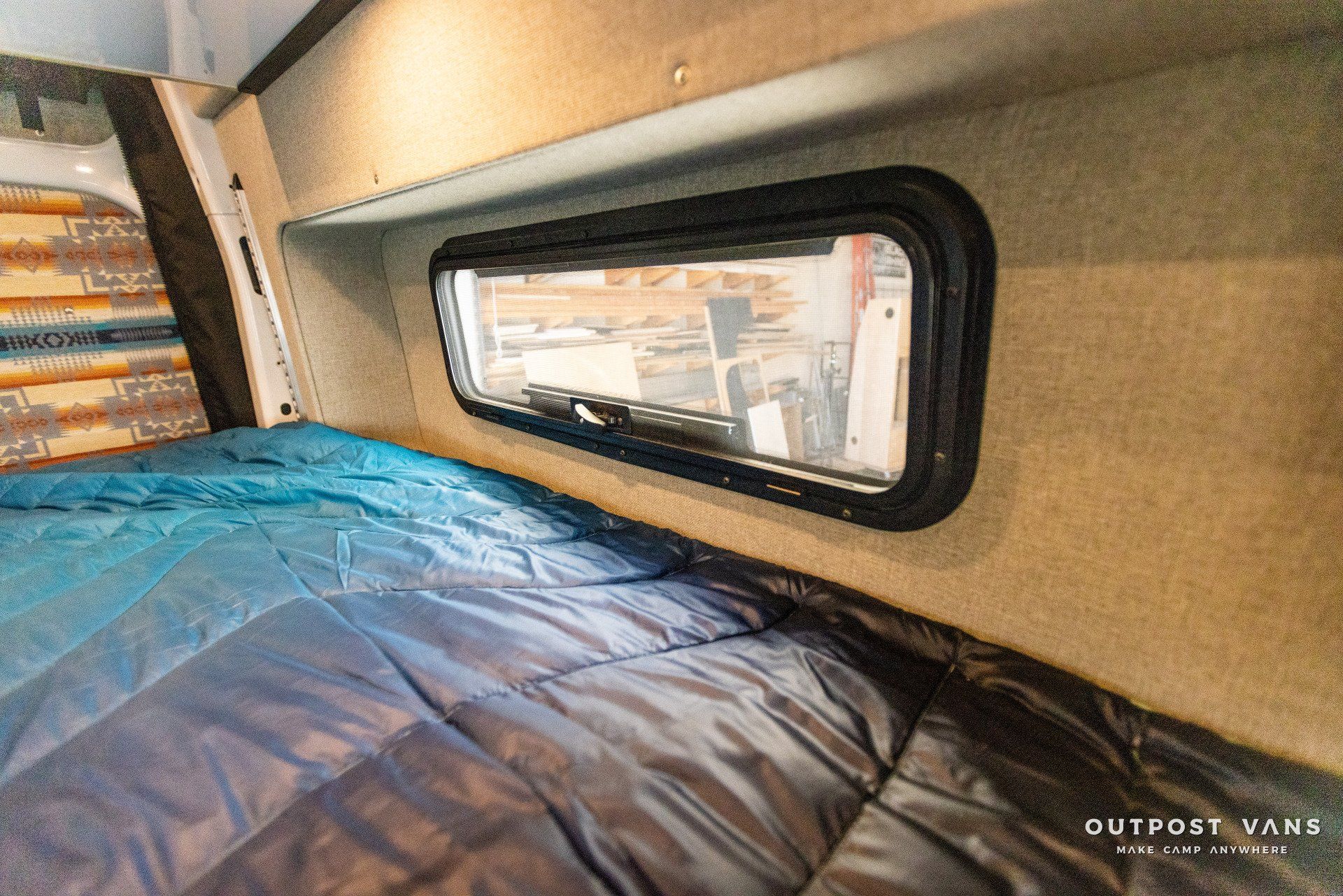 a bed with a blue blanket and a window in a van .