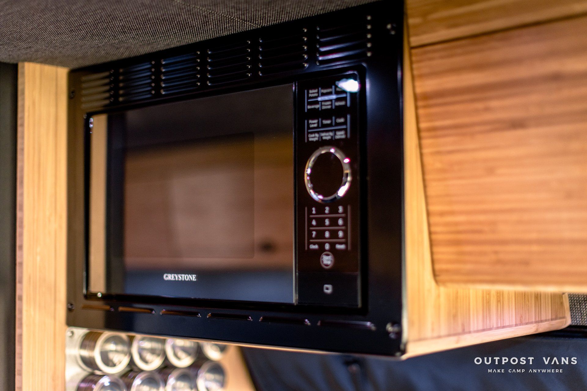 A microwave oven is hanging from the ceiling of a camper van.