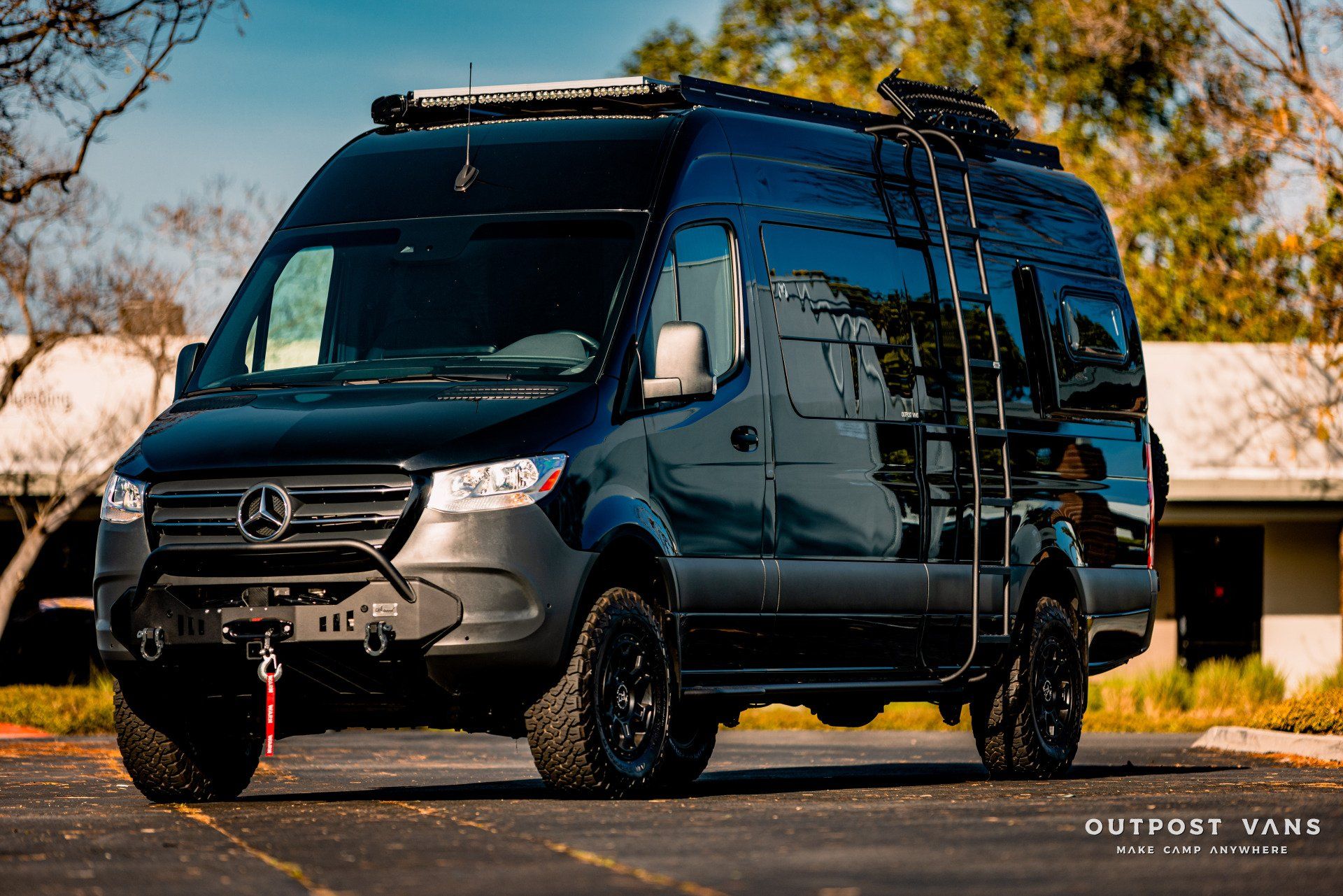 A black van with a ladder on the roof is parked in a parking lot.