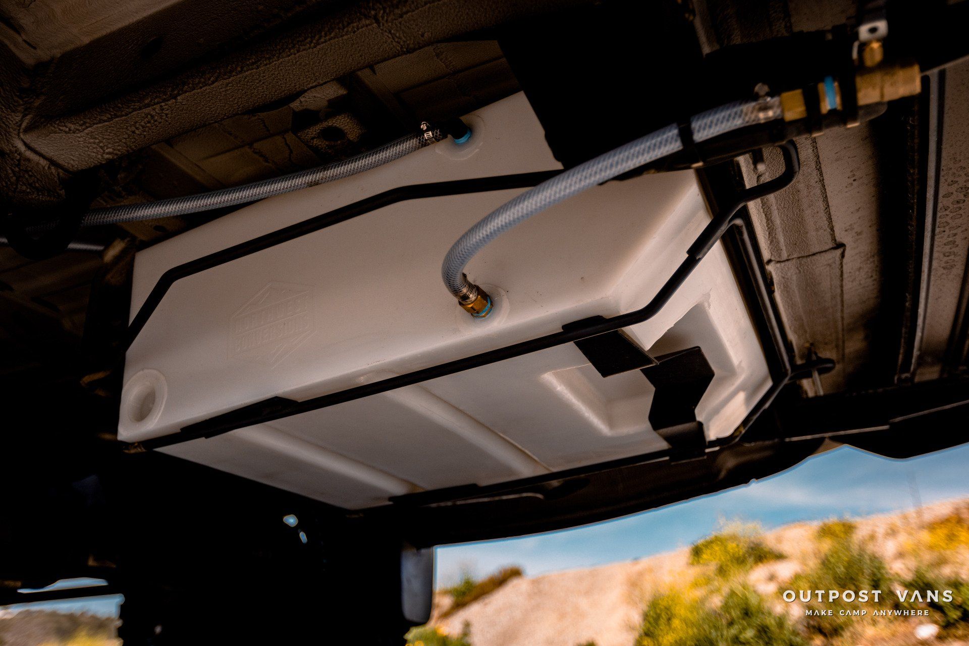 A large white tank is attached to the underside of a vehicle.