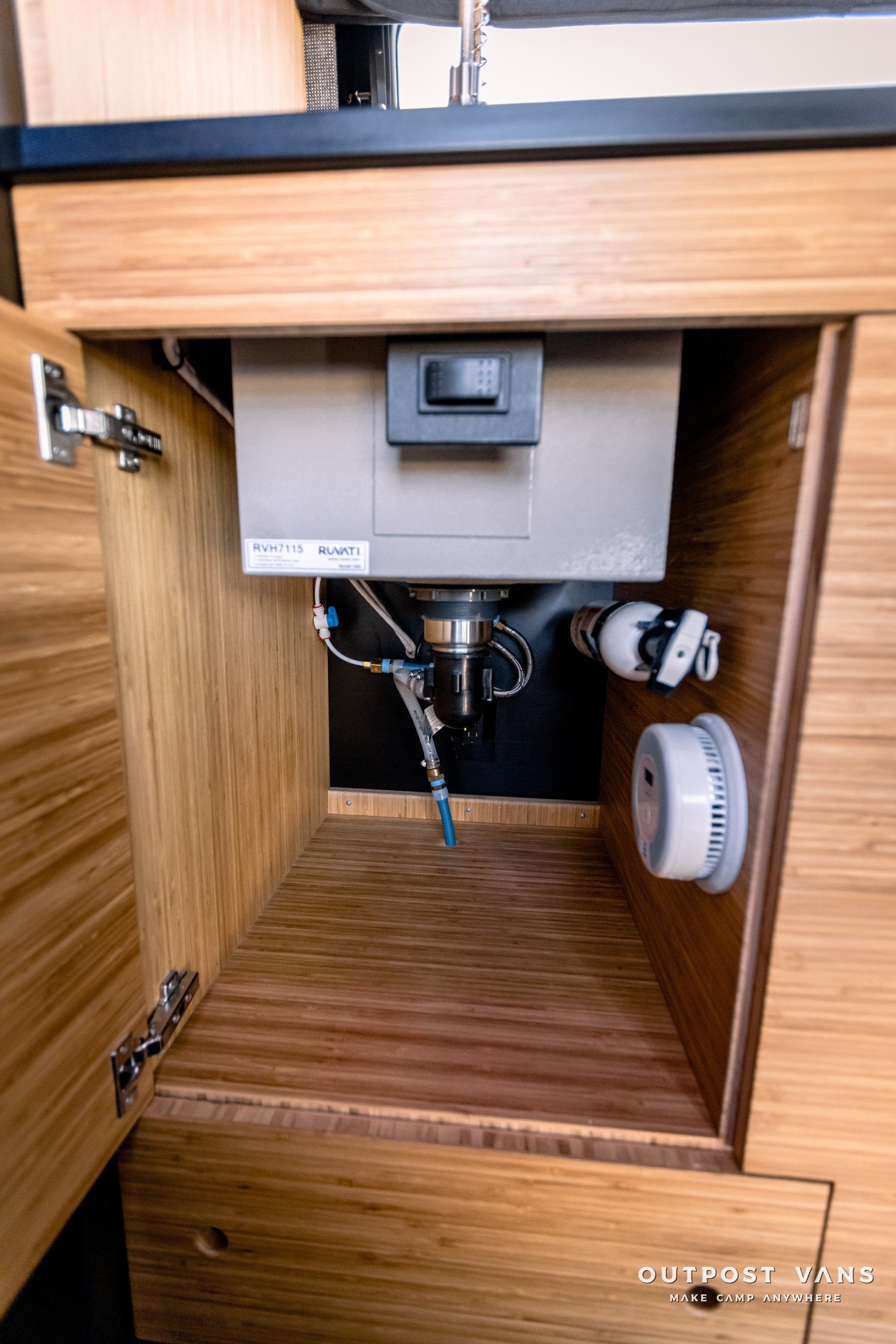 A sink is under a wooden cabinet in a kitchen.
