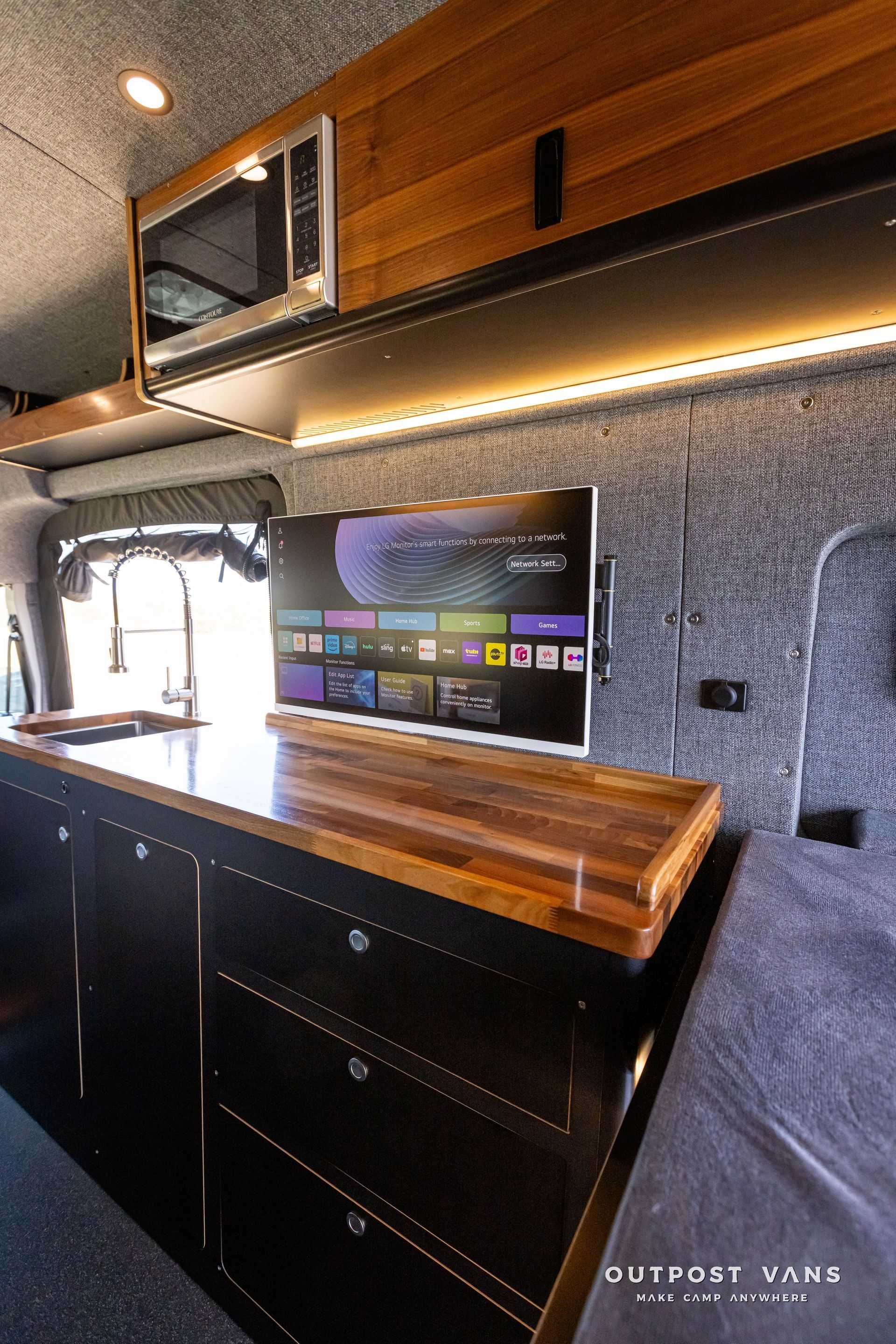 Outpost Vans custom built camper van Ford Transit 148 AWD. A kitchen in a van with a flat screen tv on the counter.