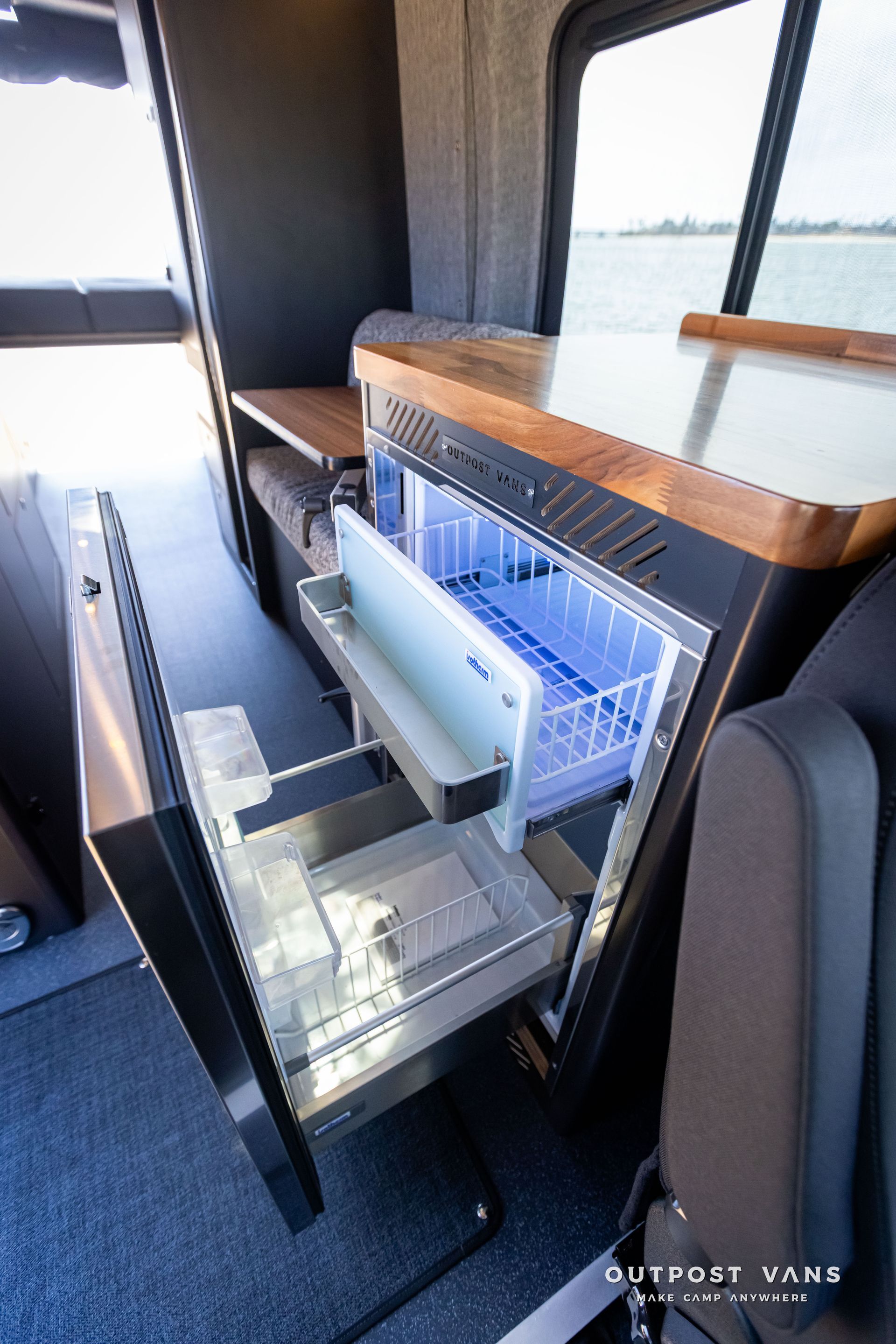 Outpost Vans custom built camper van Ford Transit 148 AWD. A stainless steel refrigerator is open in a van.