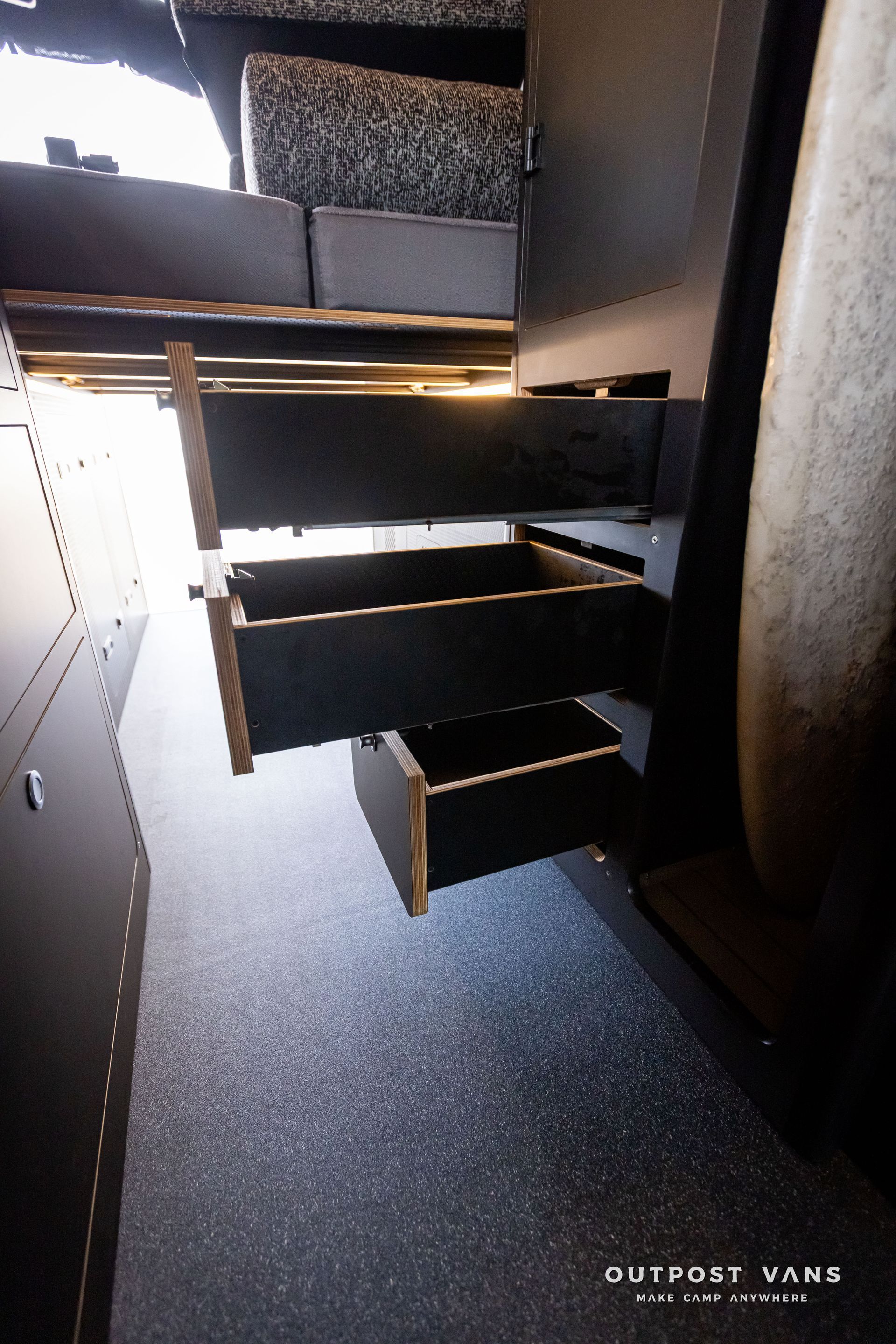 Outpost Vans custom built camper van Ford Transit 148 AWD. A row of drawers in a van with the word outpost vans on the bottom