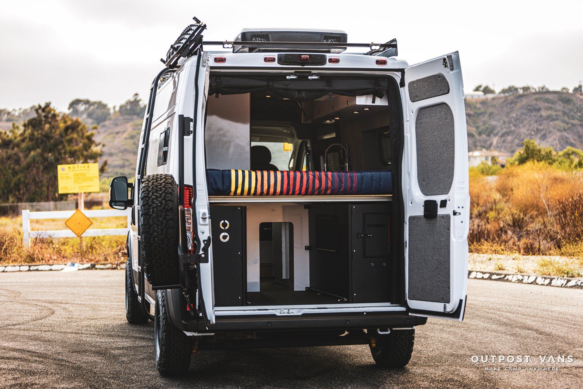 A white van is parked on the side of the road with its doors open.