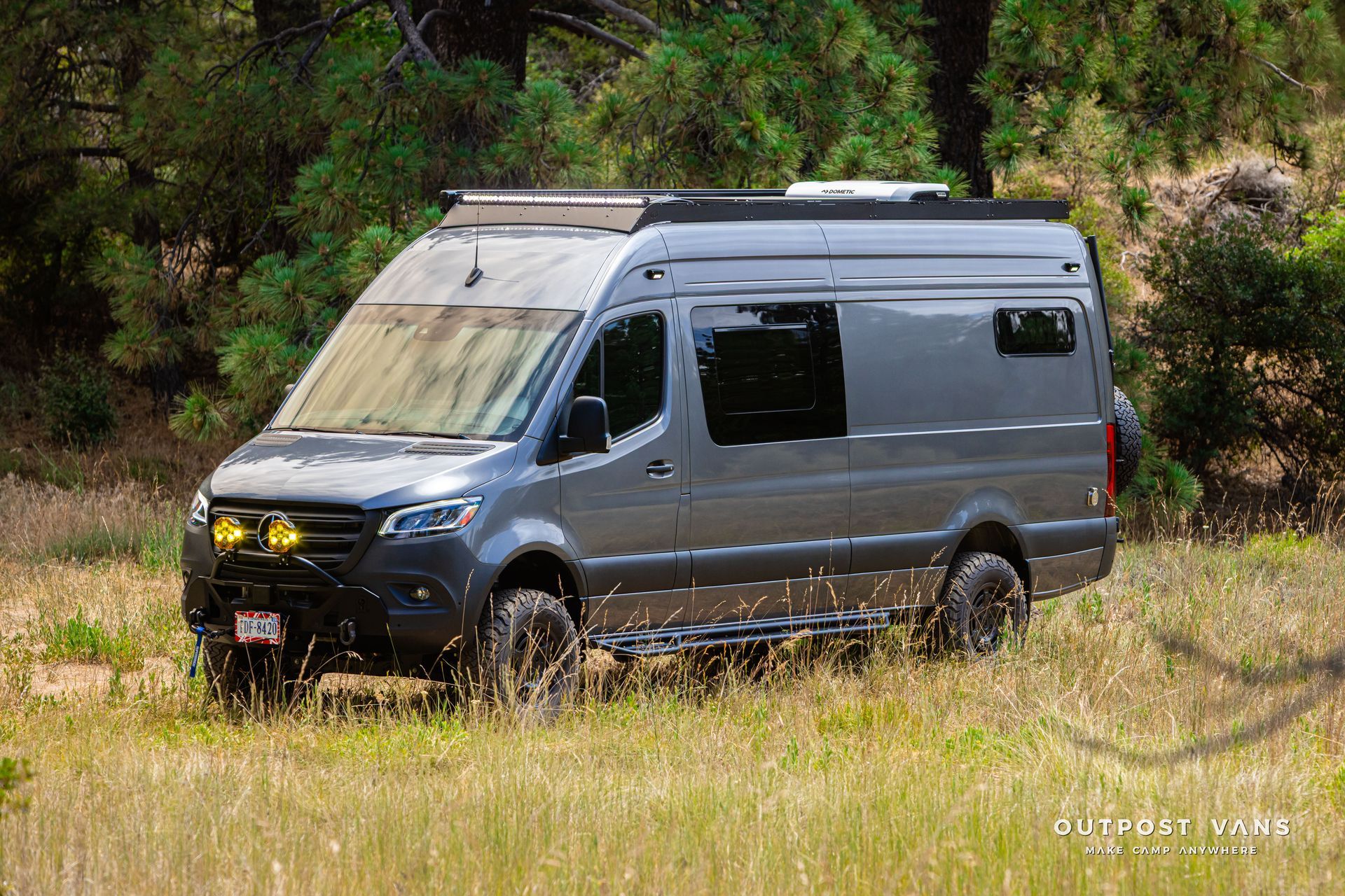 A gray van is parked in a grassy field. Outpost vans Sprinter 170 AWD.