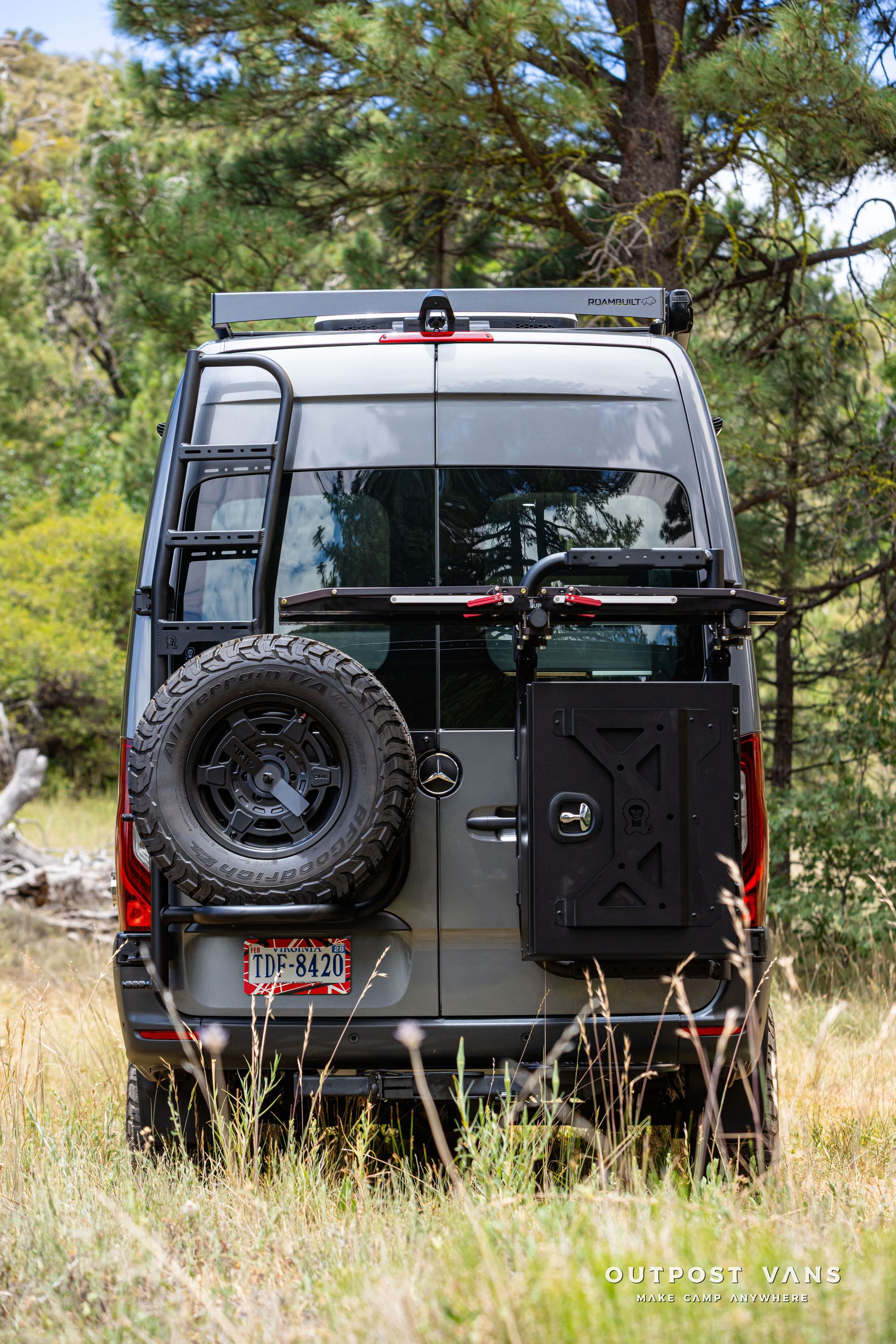 A van is parked in a field with trees in the background. Outpost vans Sprinter 170 AWD.