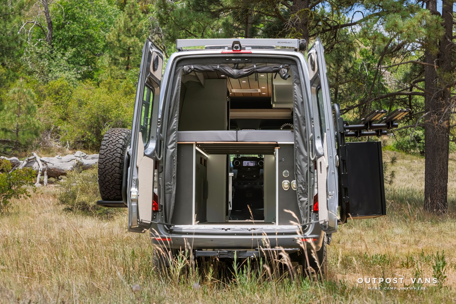 A van is parked in a grassy field with its doors open. Outpost vans Sprinter 170 AWD.