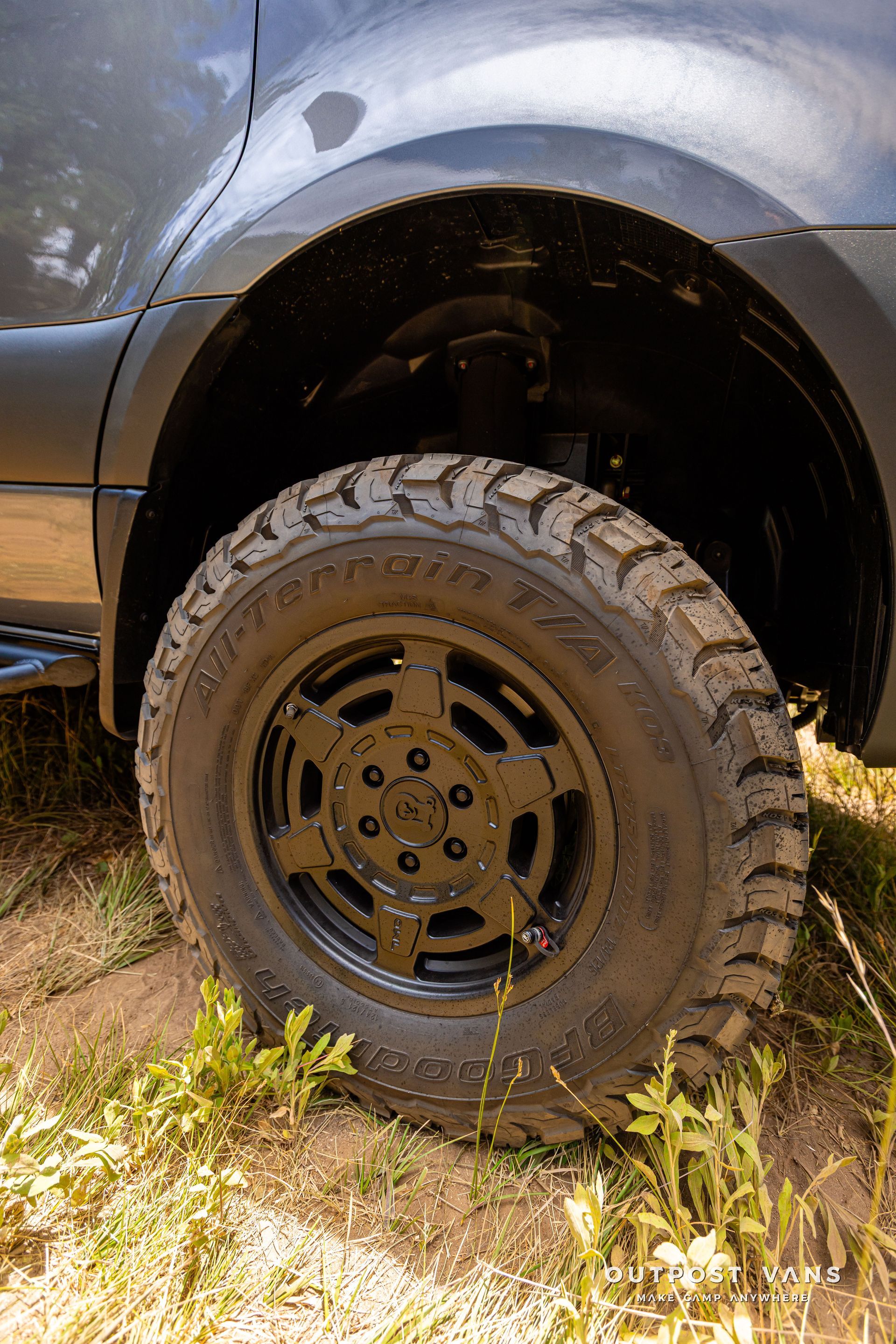 A close up of a tire on a car on a dirt road. Outpost vans Sprinter 170 AWD.