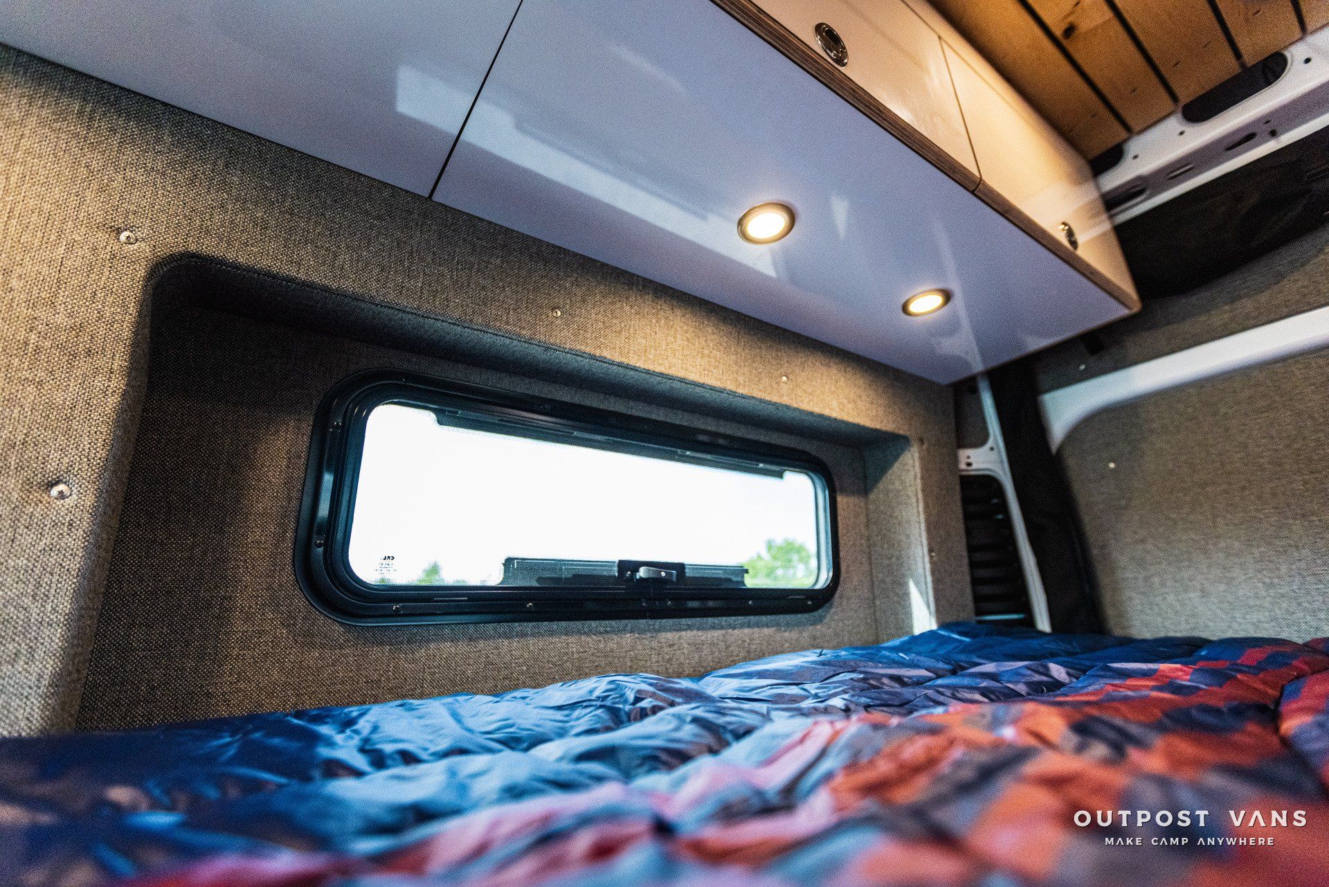 A bed in a van with a window on the wall.
