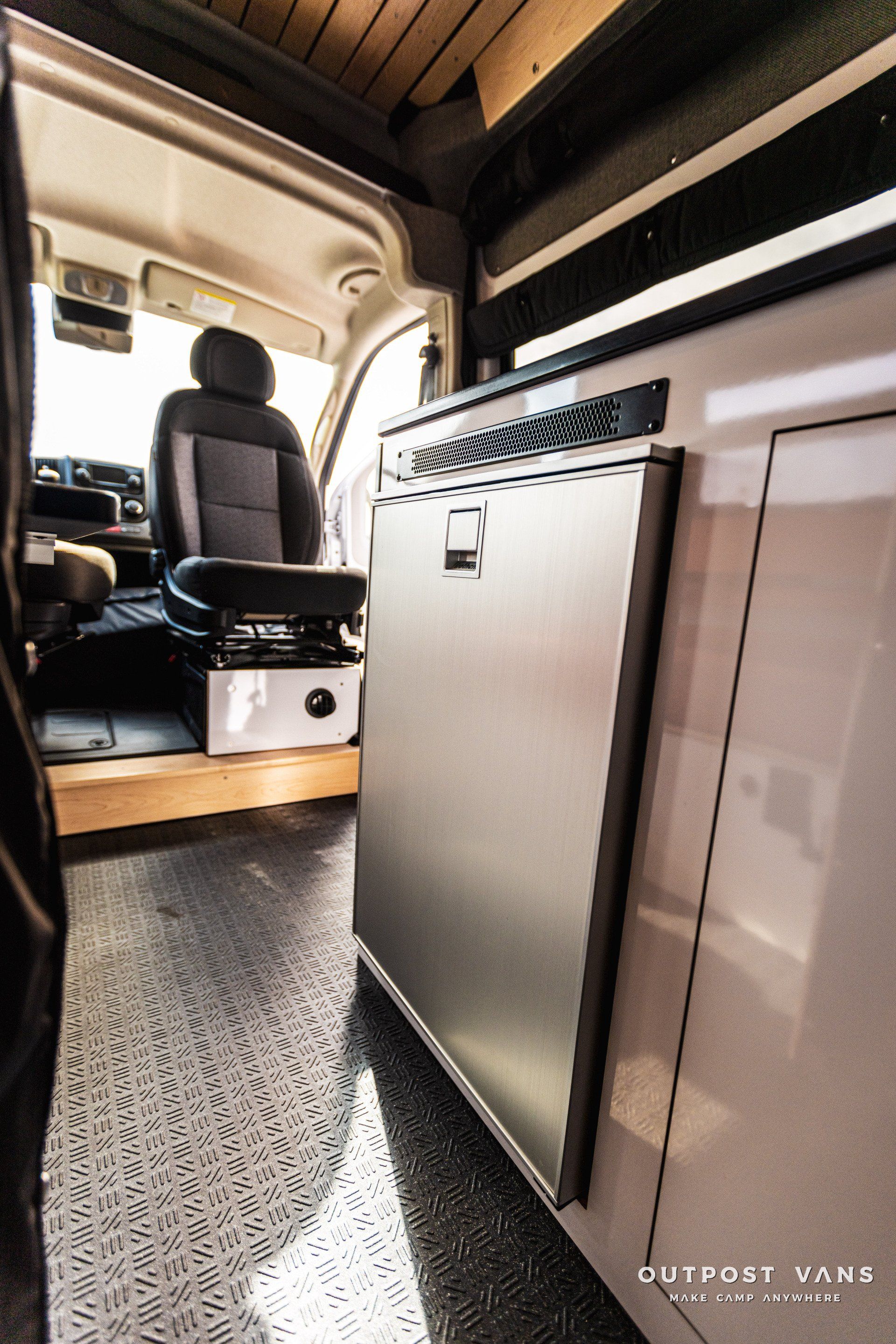 The inside of a camper van with a refrigerator and a seat.
