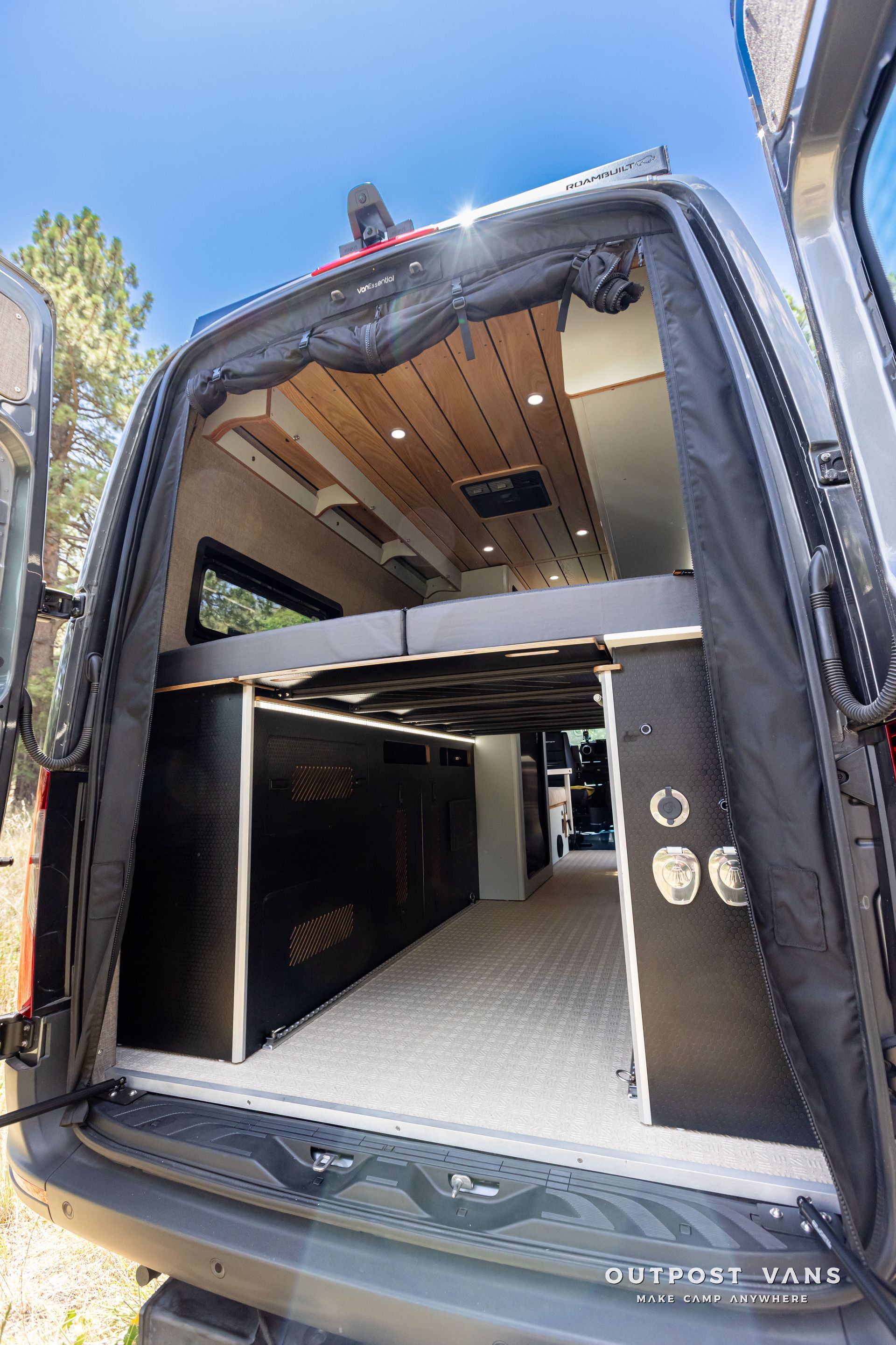 The back of a van with the door open and a bed in the back. Outpost vans Sprinter 170 AWD.