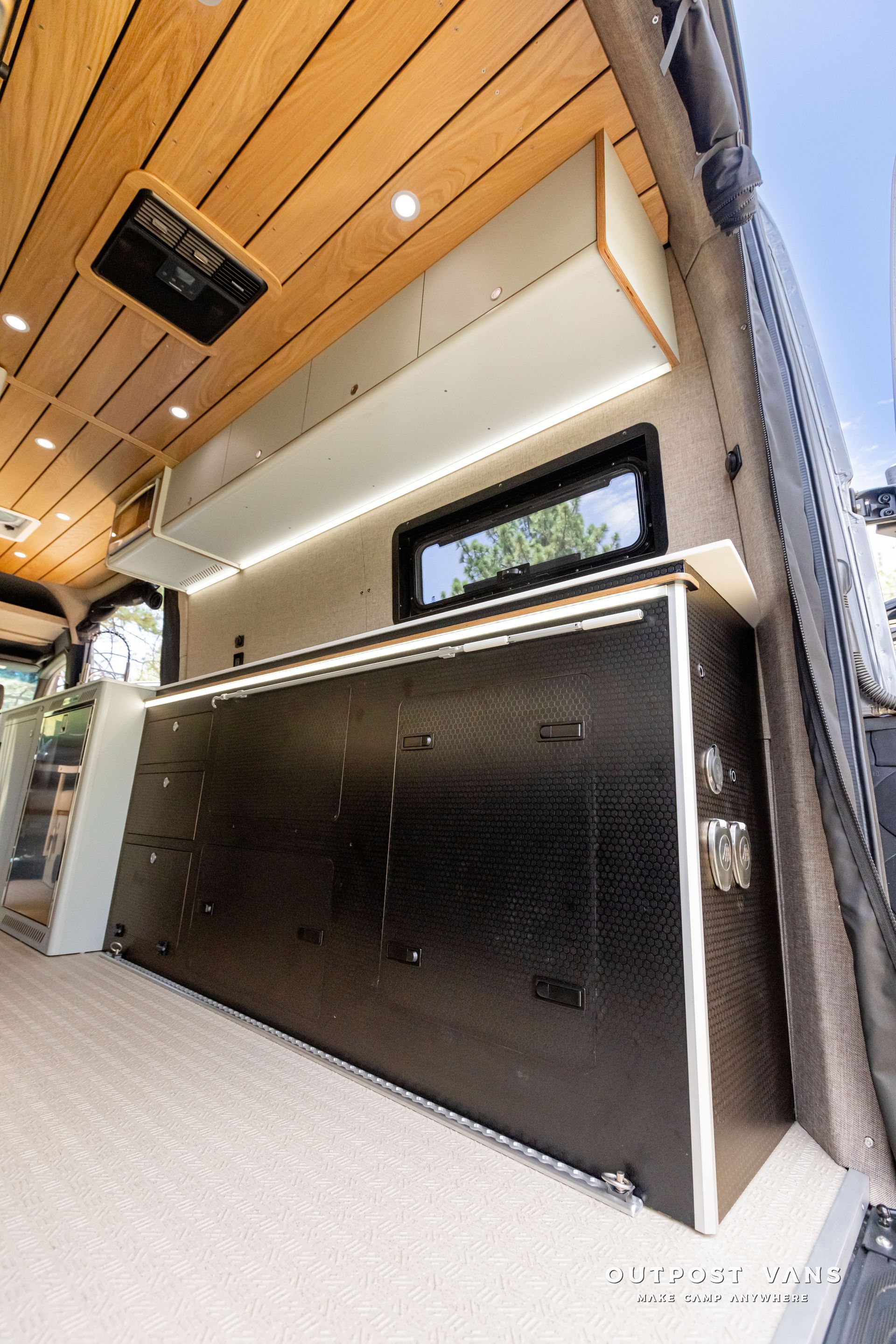 The inside of a van with a lot of cabinets and a window. Outpost vans Sprinter 170 AWD.