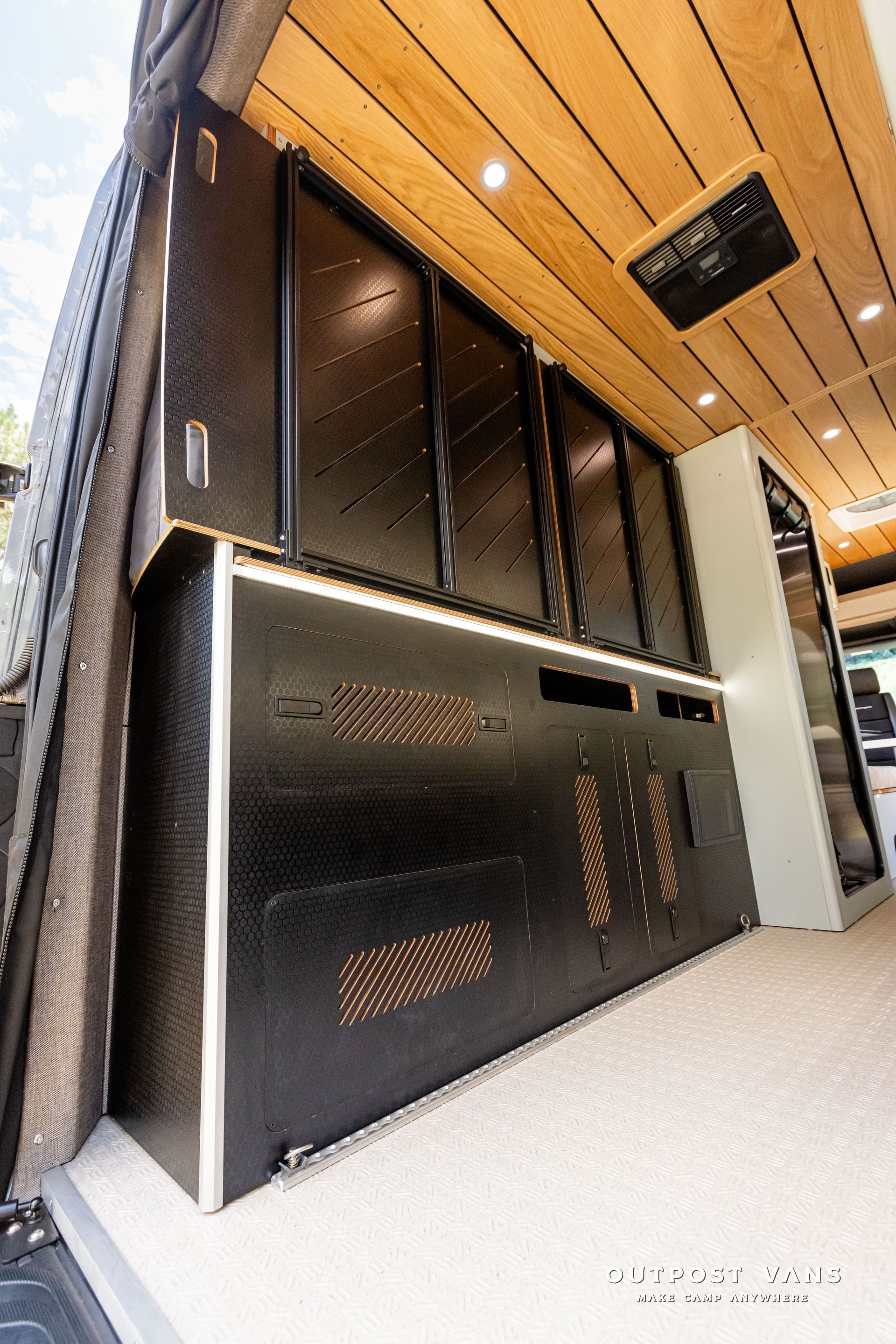 The inside of a van with a lot of cabinets and a wooden ceiling. Outpost vans Sprinter 170 AWD.