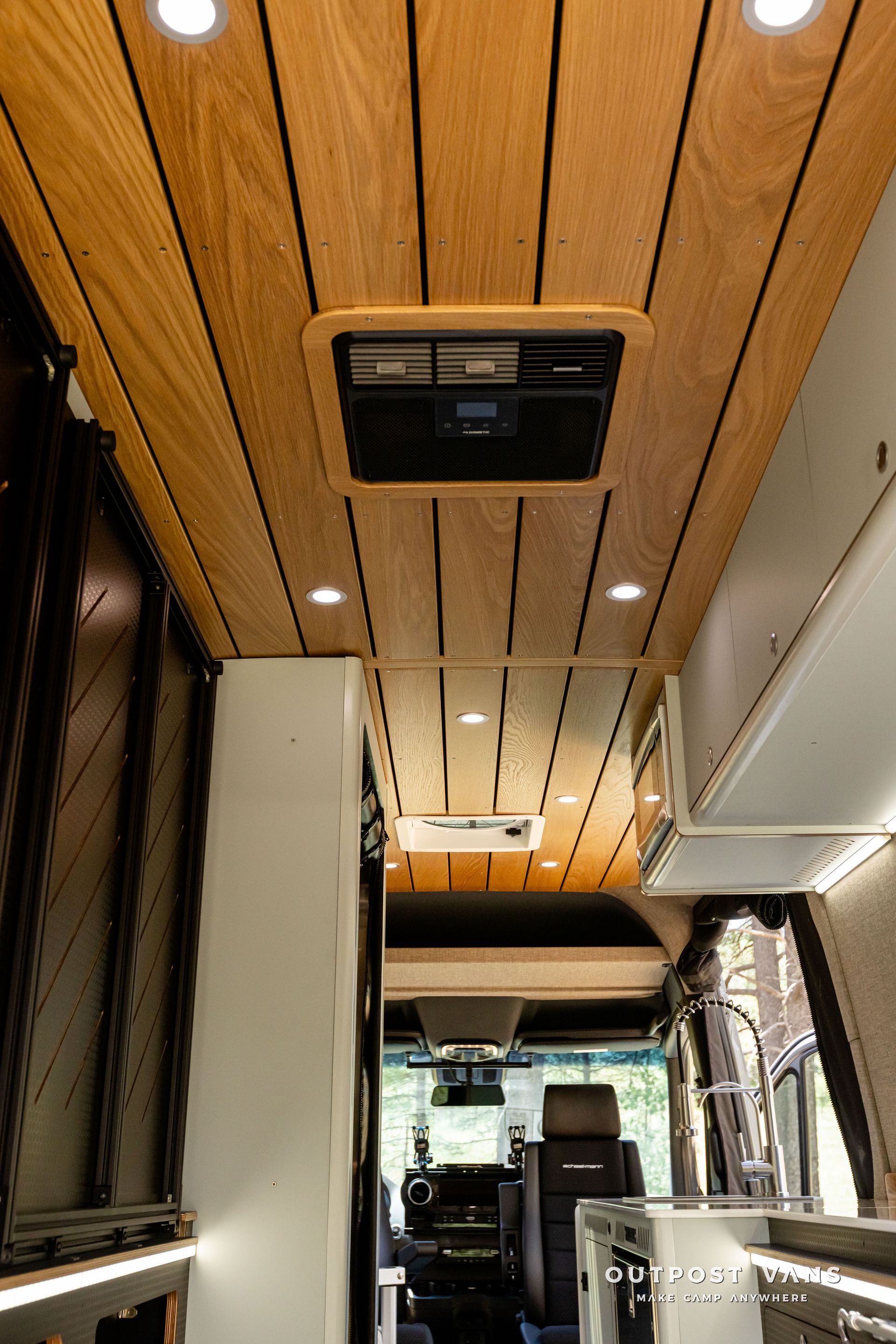 The inside of a van with a wooden ceiling and a ceiling fan. Outpost vans Sprinter 170 AWD.