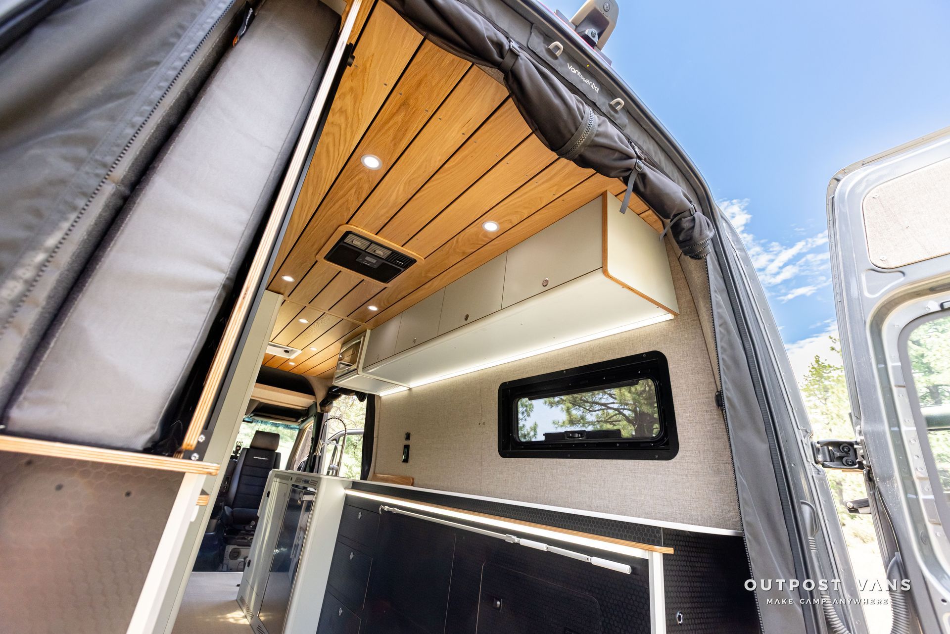 The inside of a van with the door open and a wooden ceiling. Outpost vans Sprinter 170 AWD.
