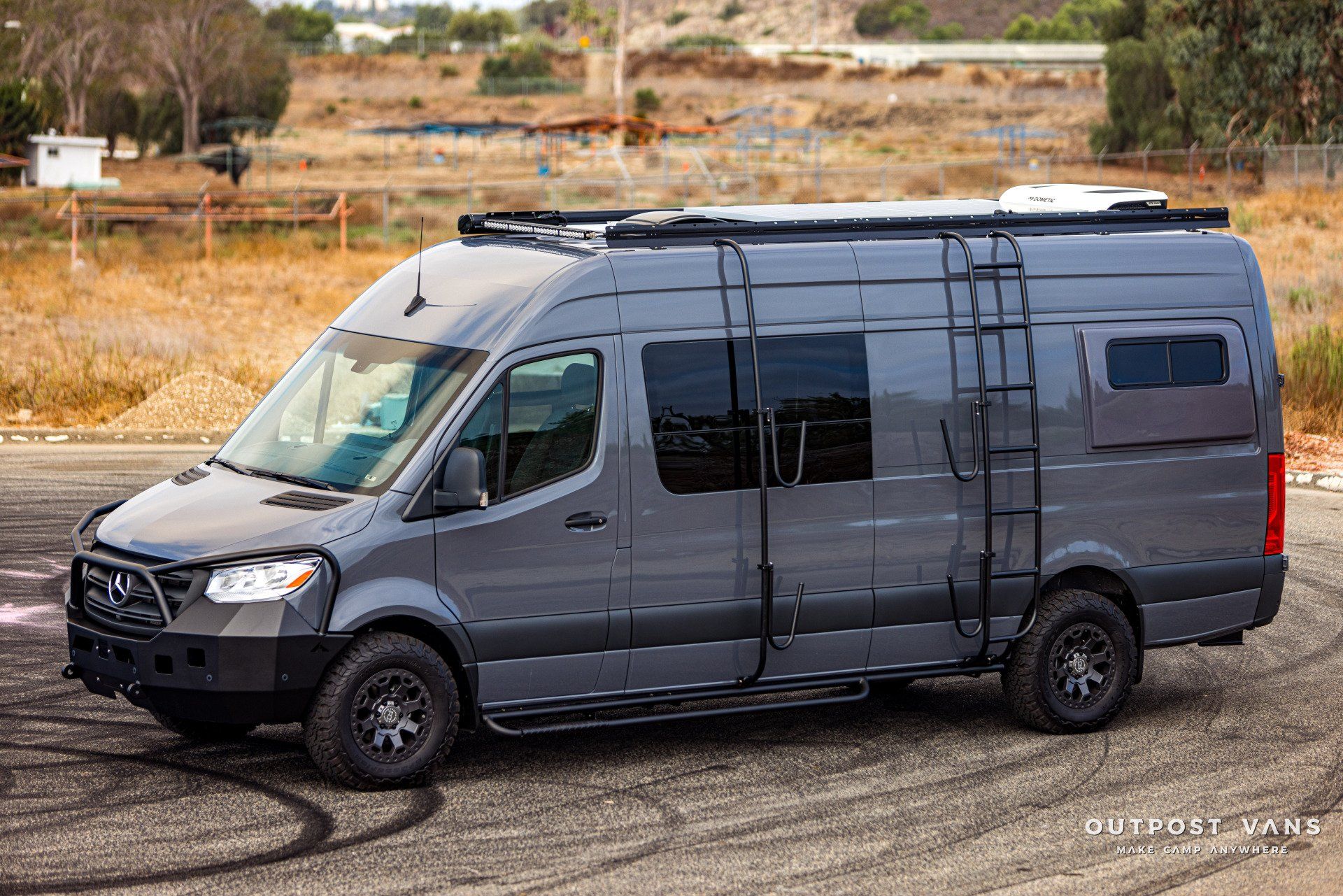 A gray van with a ladder on the side is parked on the side of the road.