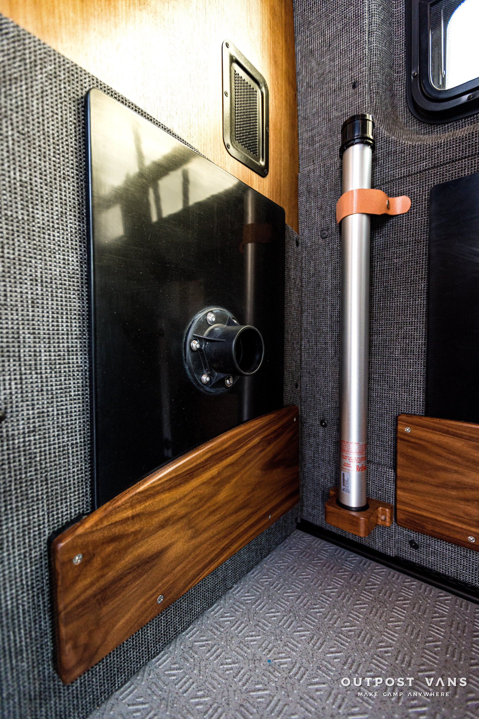 A corner of a room with a wooden shelf and a metal pole.