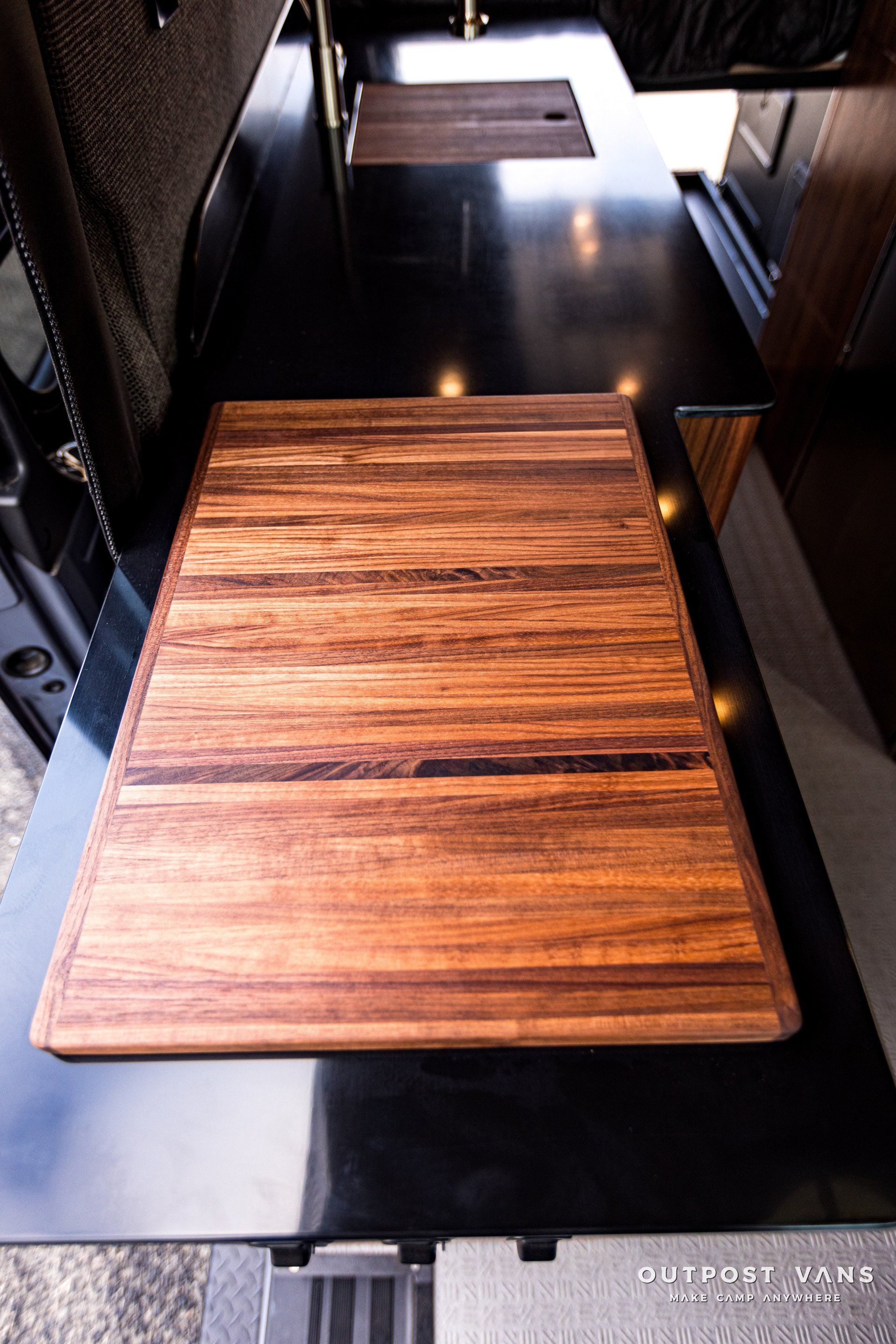 A wooden cutting board is sitting on top of a black counter in a kitchen.