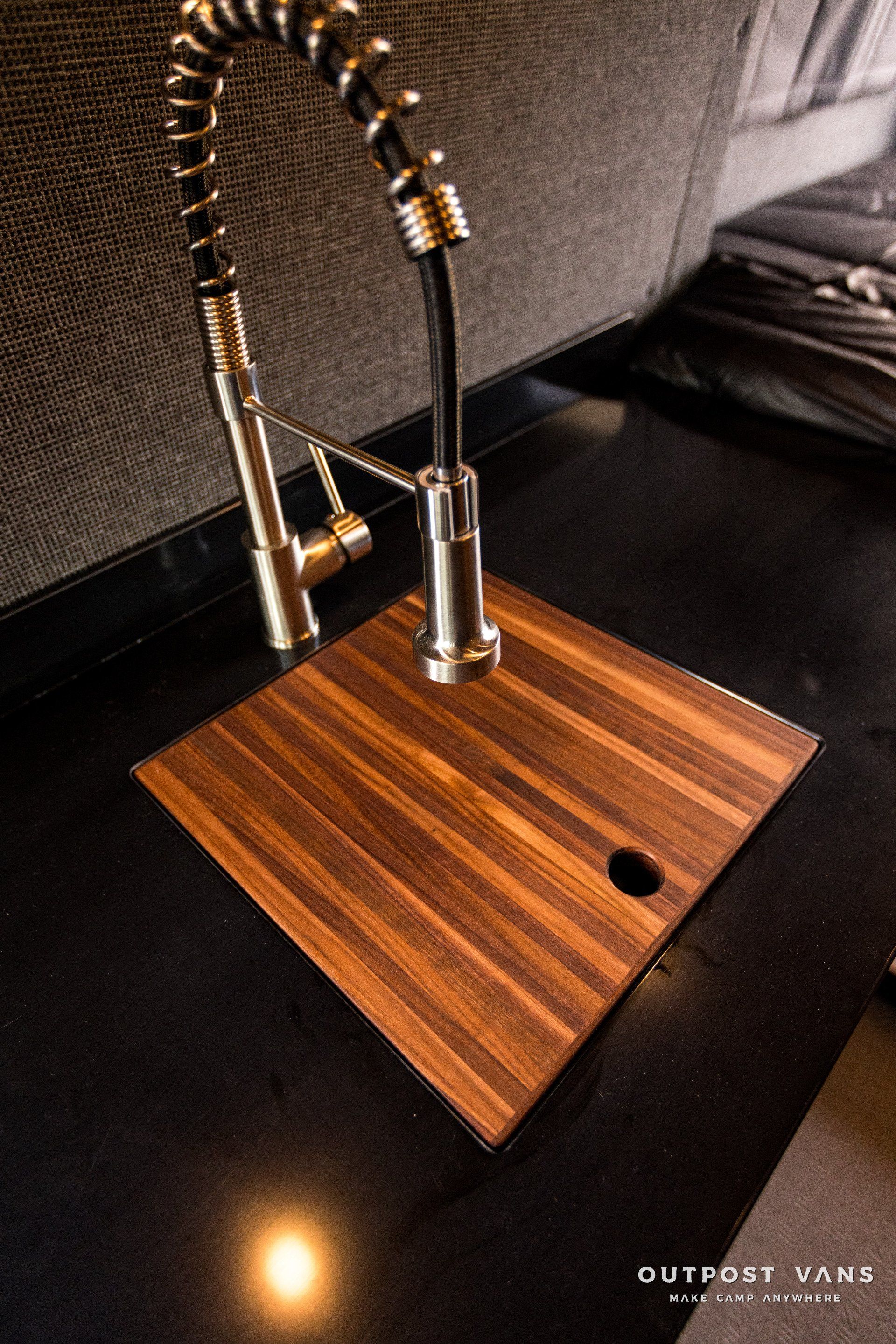 A kitchen sink with a wooden cutting board and a faucet