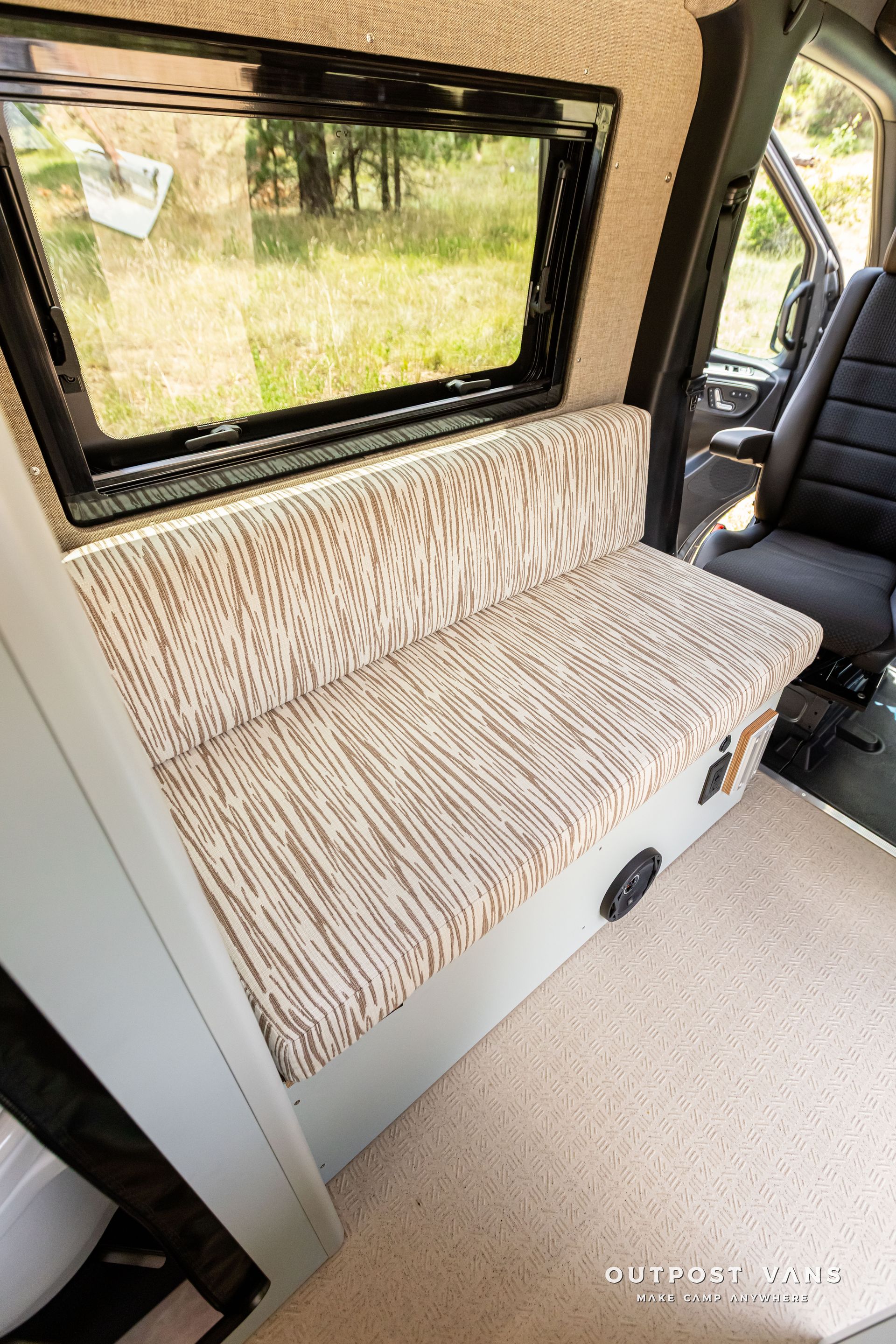 A couch in the back of a van with a window. Outpost vans Sprinter 170 AWD.