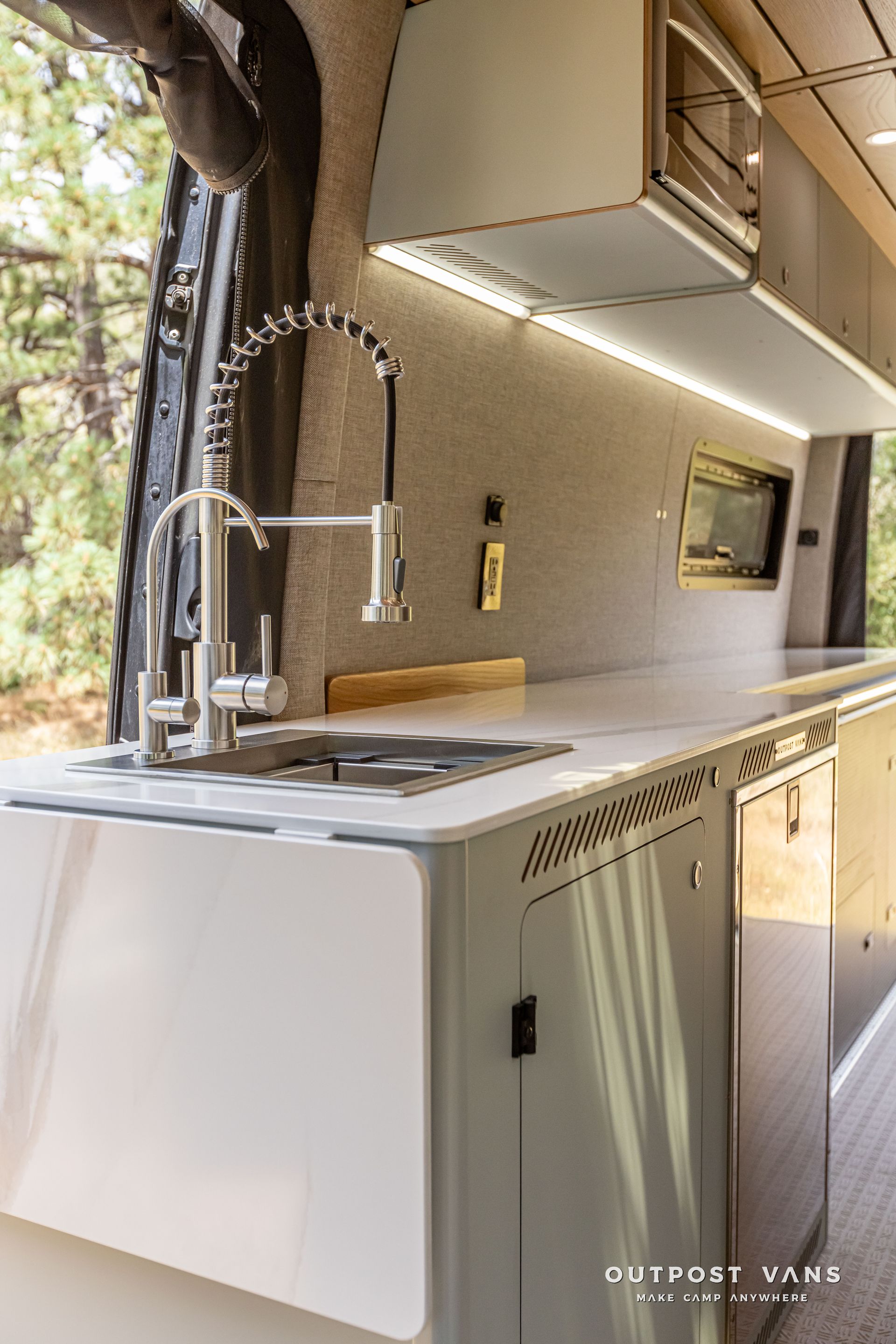A kitchen in a van with a sink and a faucet. Outpost vans Sprinter 170 AWD.