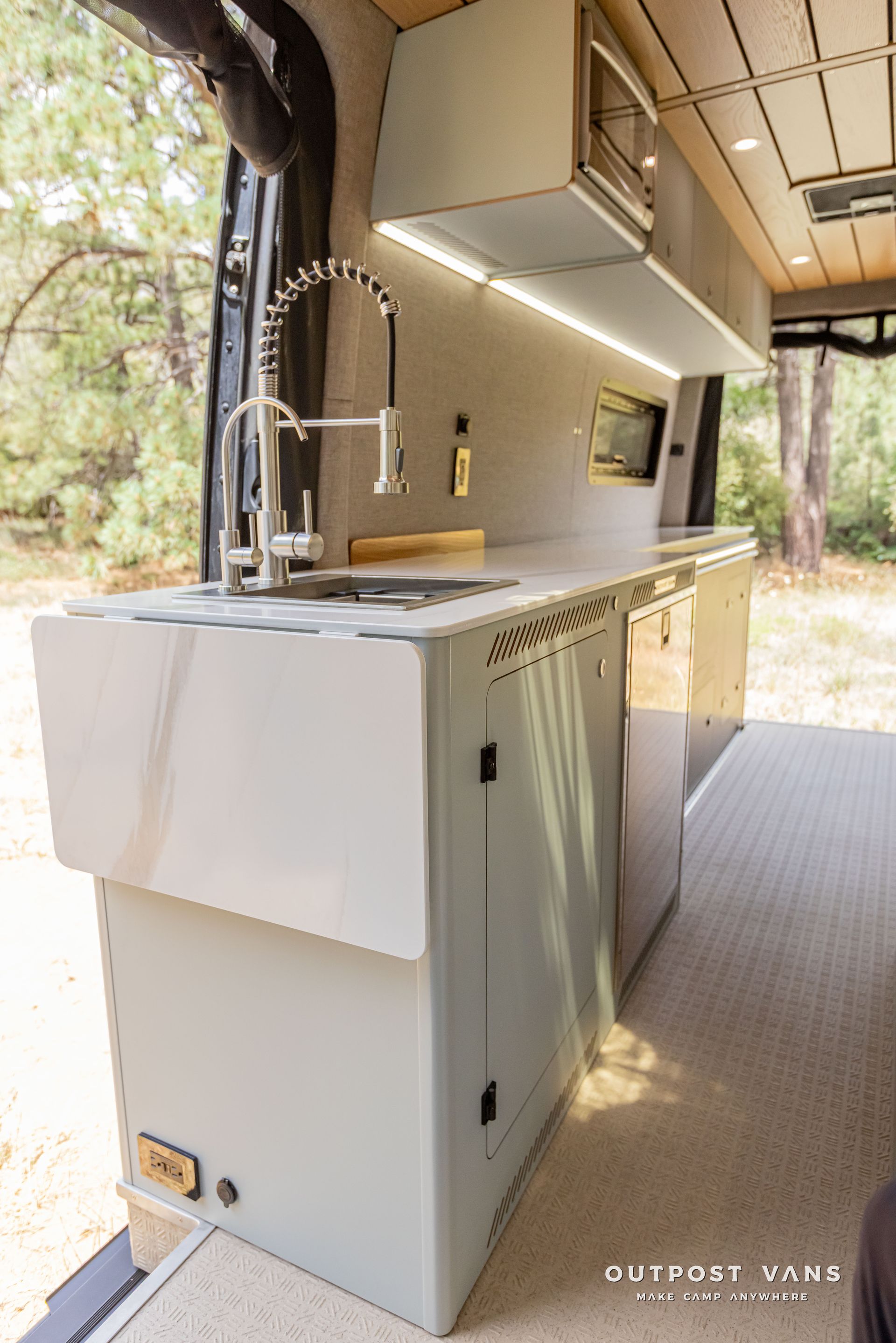 A kitchen in a van with a sink and cabinets. Outpost vans Sprinter 170 AWD.
