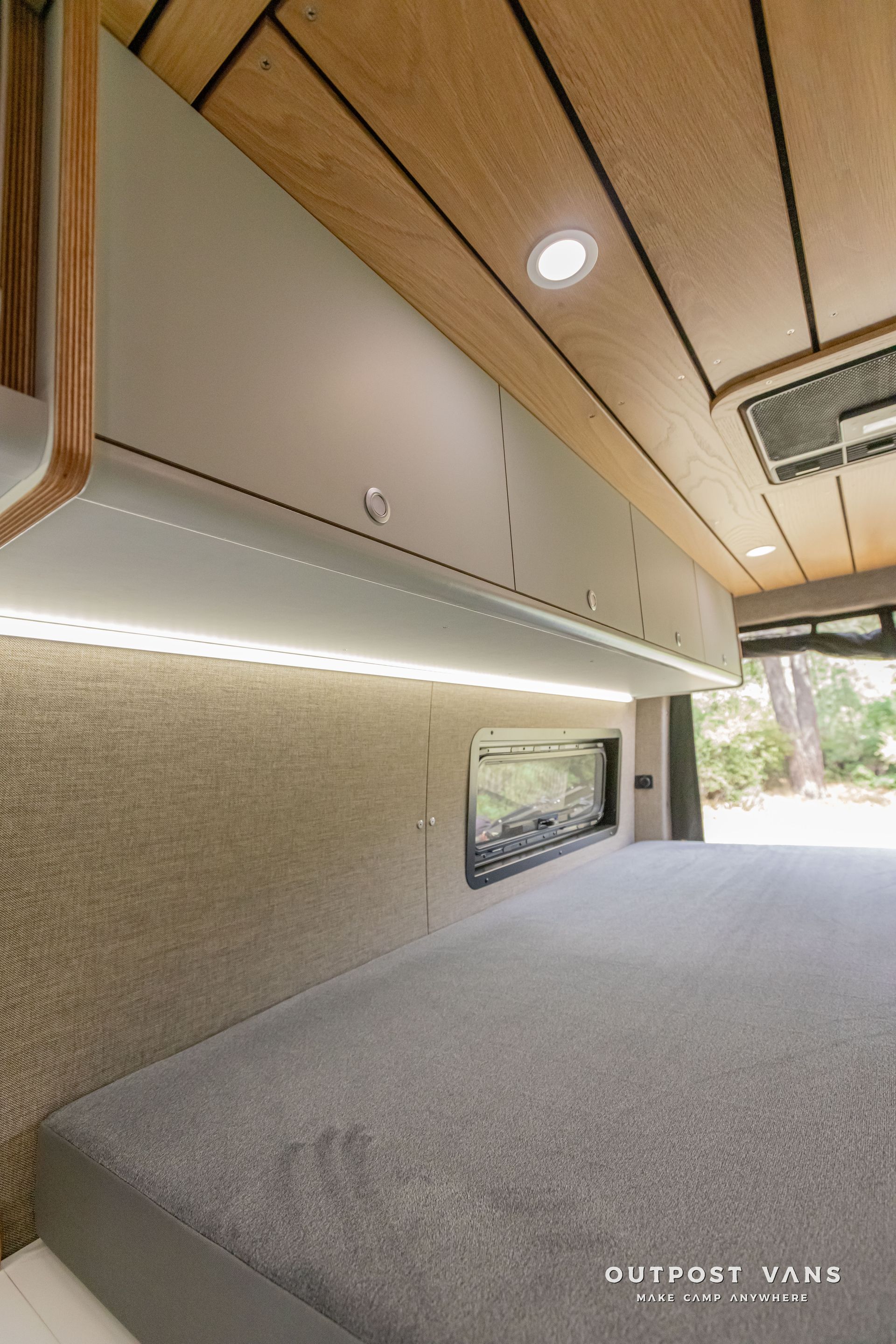 The inside of a camper van with a bed and cabinets. Outpost vans Sprinter 170 AWD.