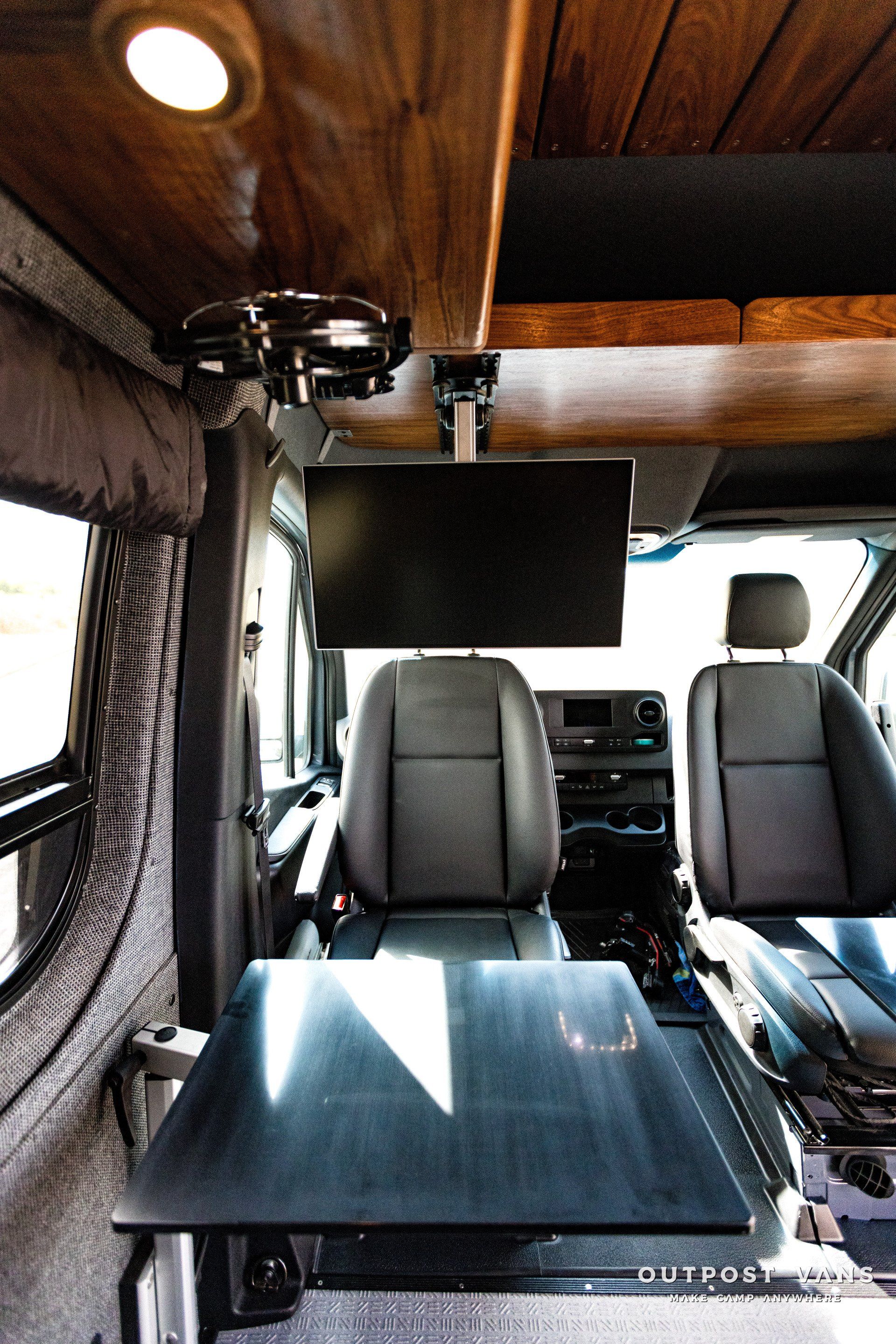 The inside of a van with a table and a tv on the ceiling.