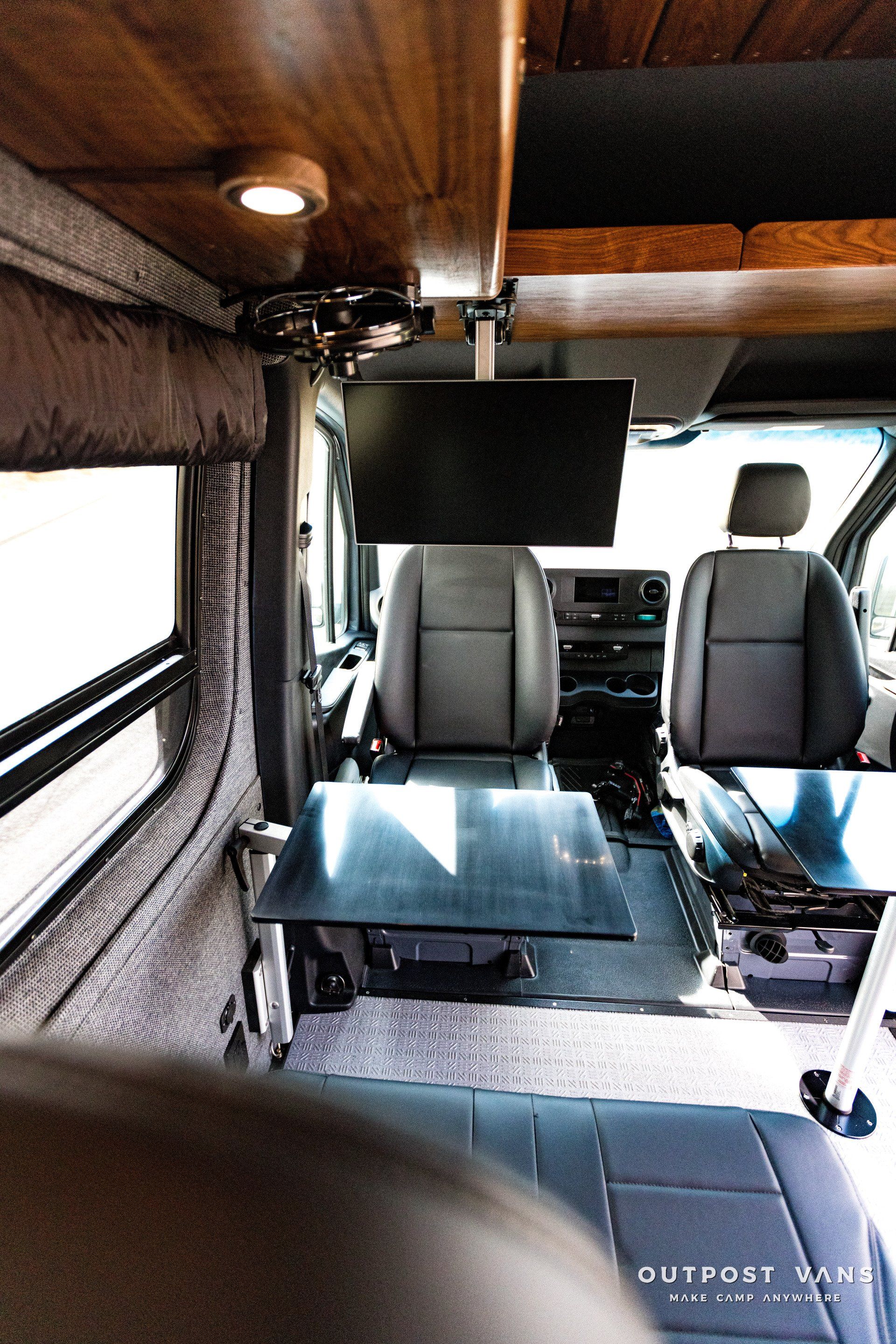 The inside of a van with a table and a tv on the ceiling.