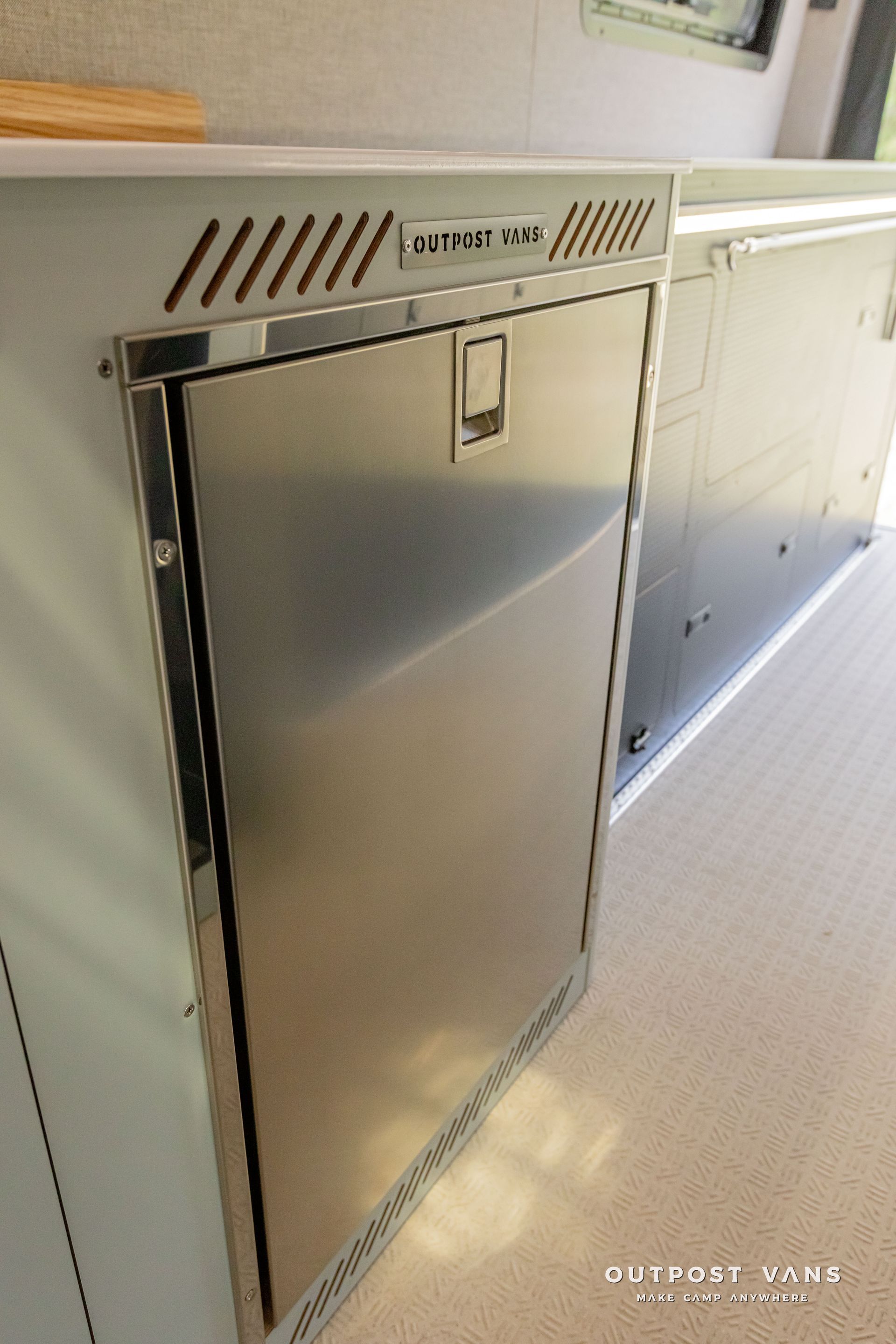 A stainless steel refrigerator is built into the wall of a kitchen. Outpost vans Sprinter 170 AWD.