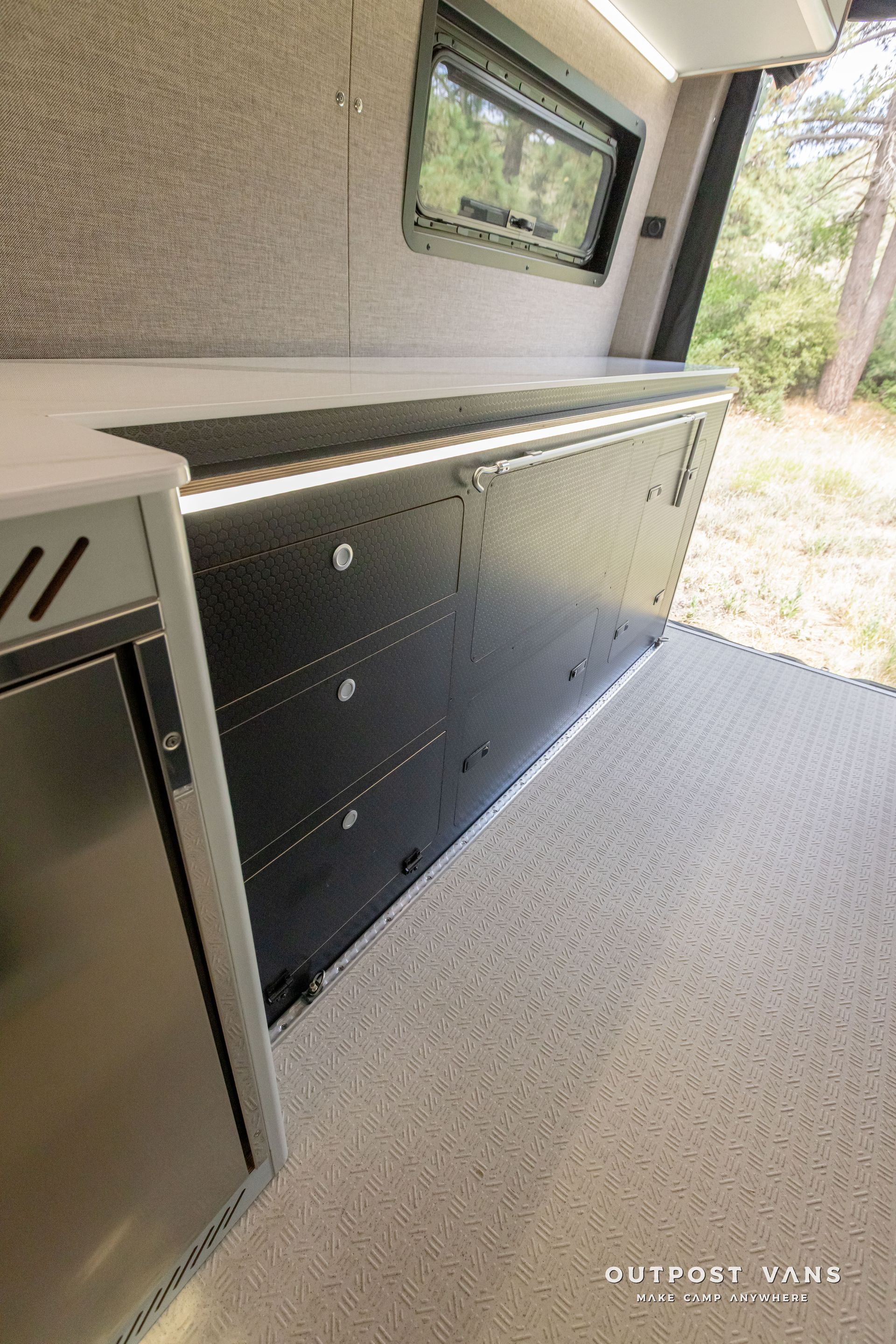 A kitchen in a van with stainless steel appliances and a refrigerator. Outpost vans Sprinter 170 AWD.