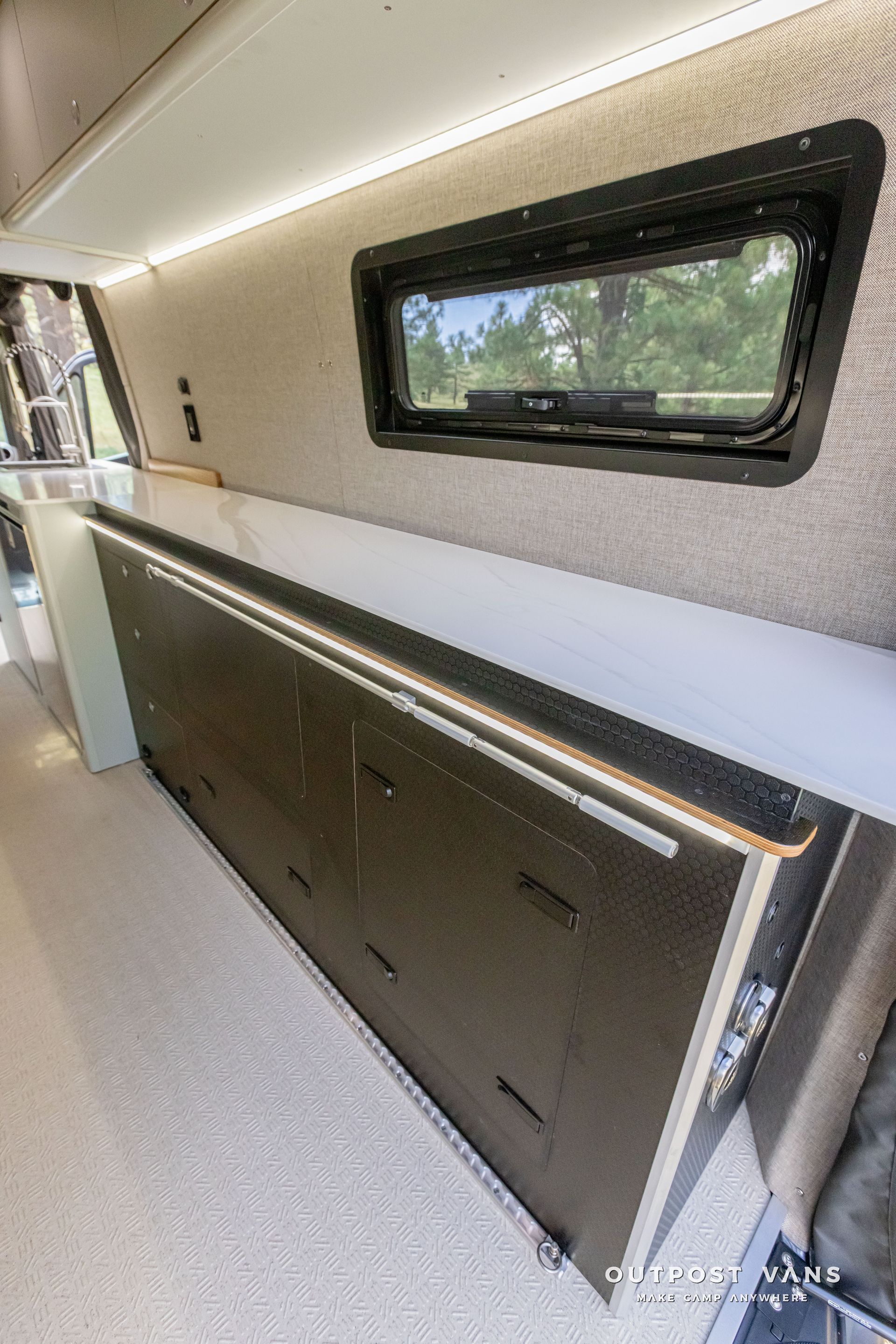 A kitchen in a van with a large cabinet and a window. Outpost vans Sprinter 170 AWD.