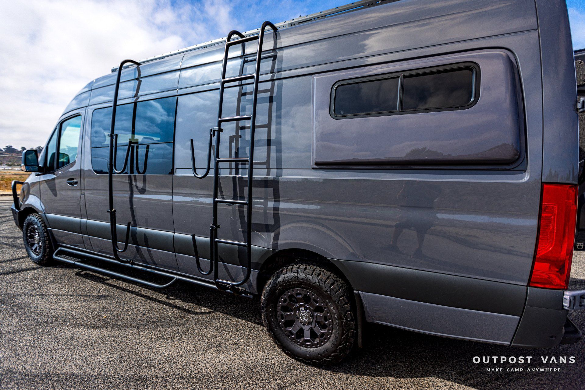 A gray van with a ladder attached to the side is parked on the side of the road.