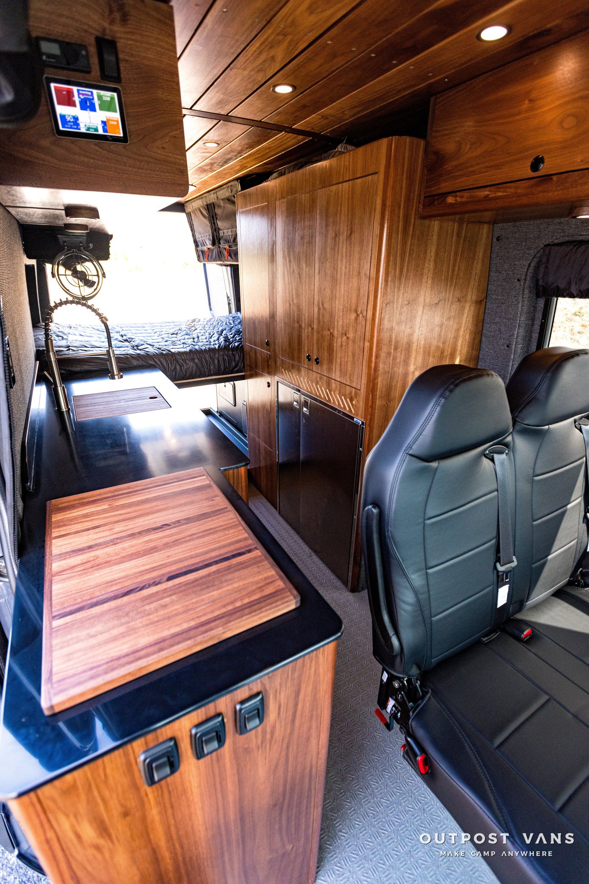 The inside of a camper van with wooden cabinets and black seats.