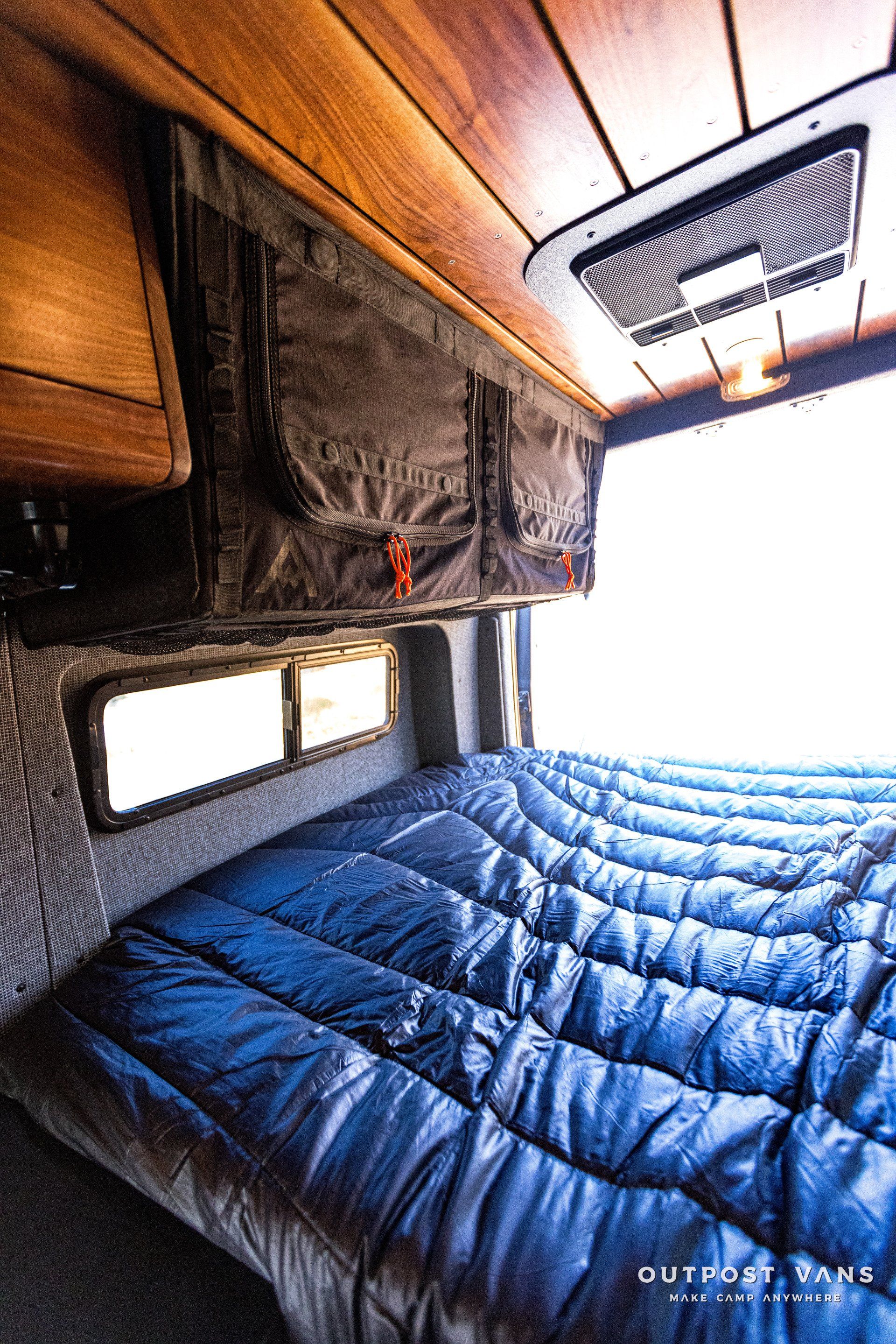 A bed in a van with a blue blanket on it.