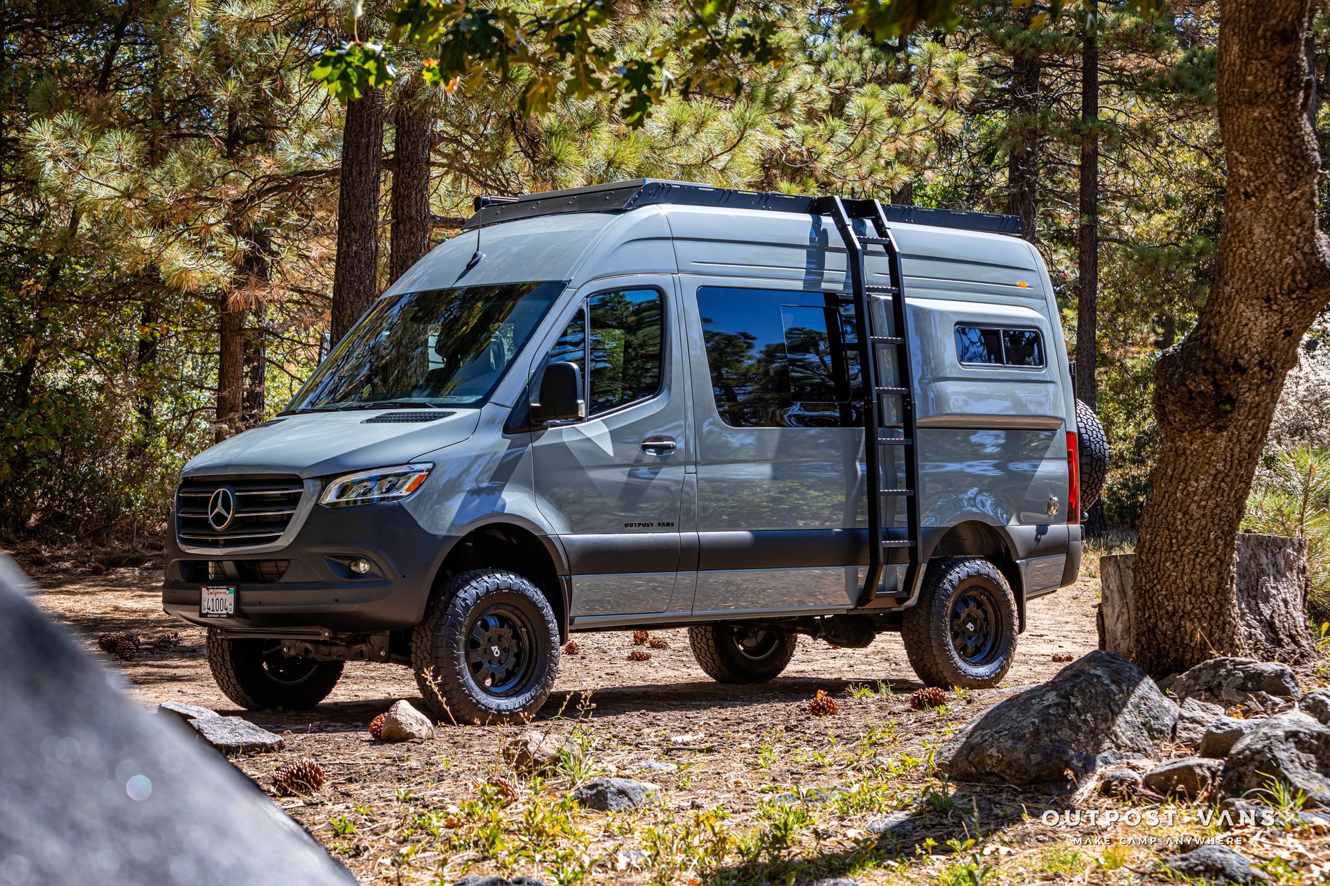 Sprinter Gray camper van with black ladder parked in a forest.